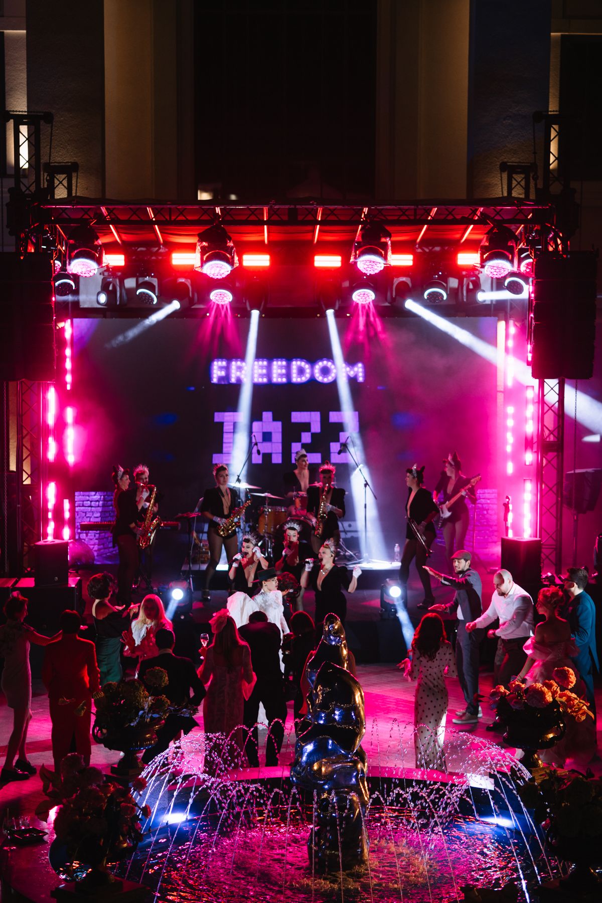 Nightclub scene with pink and purple lighting illuminating a dance floor and stage area with fountains and crowd.