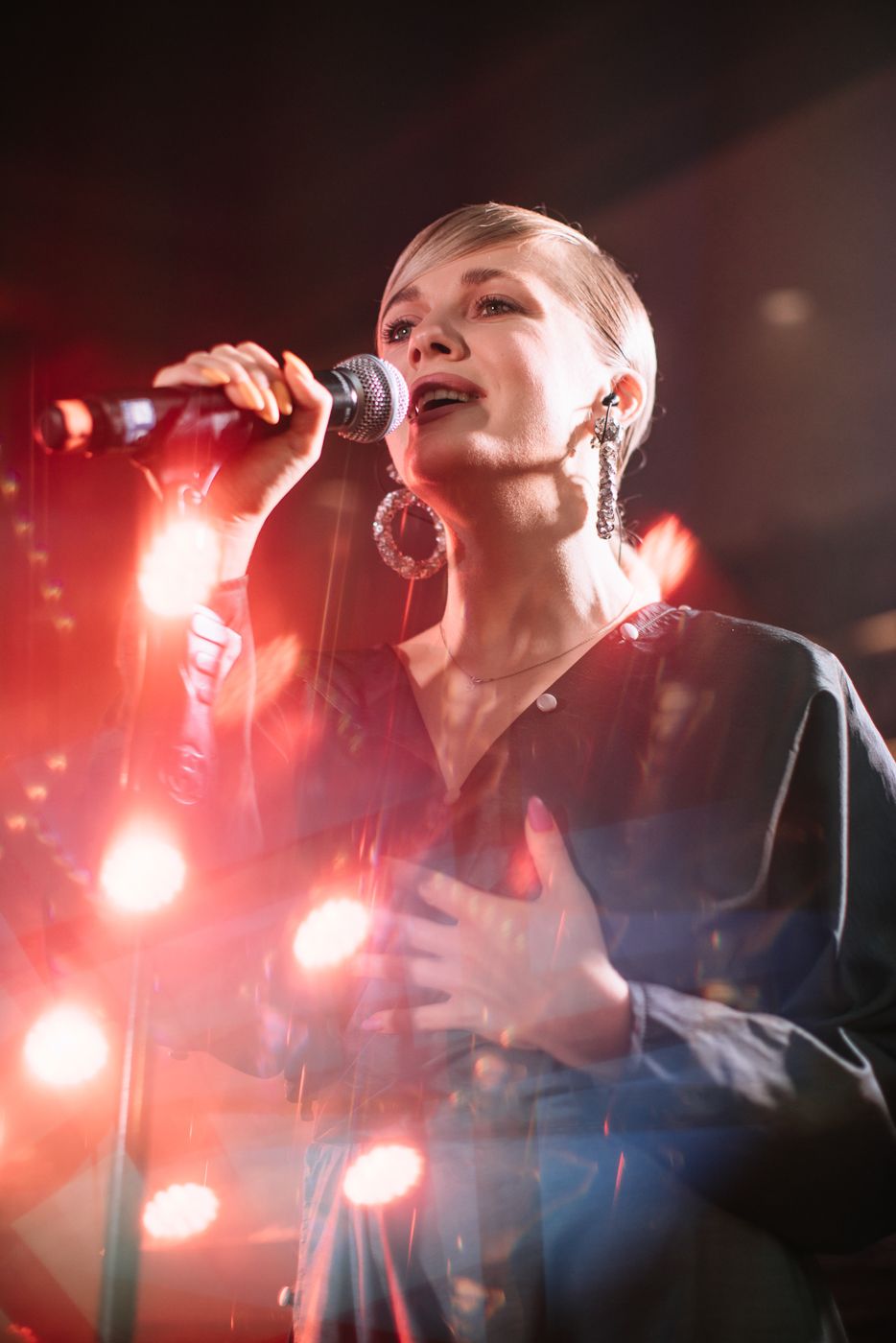 Concert performer singing passionately under dramatic red stage lighting.