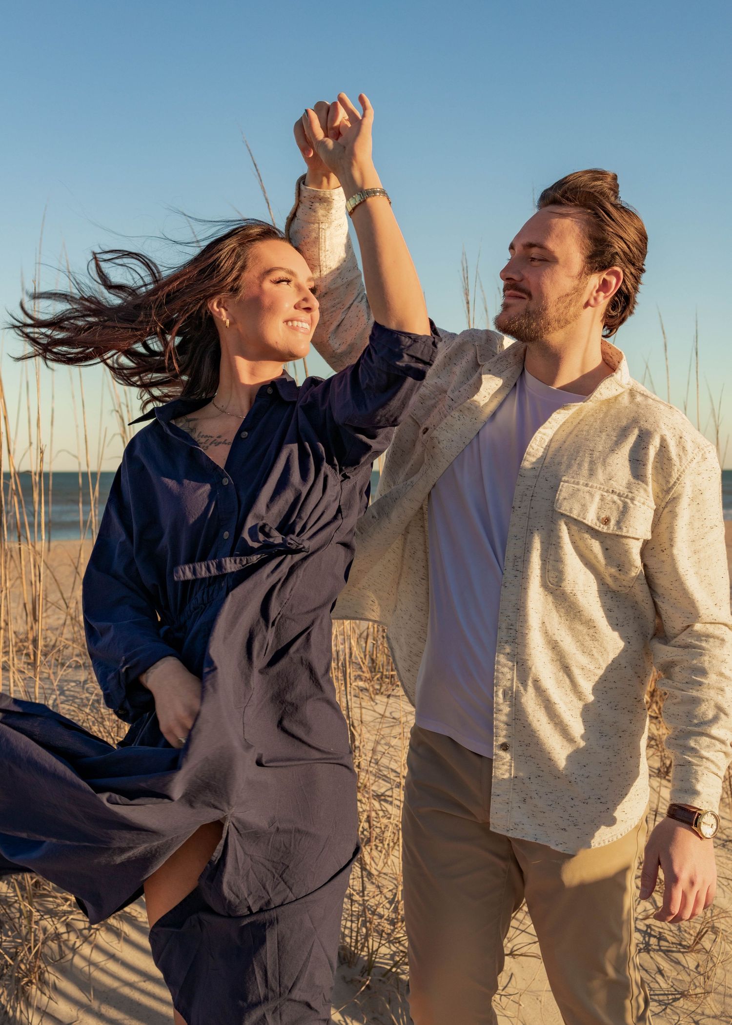 Couple dances playfully together on beach at sunset.