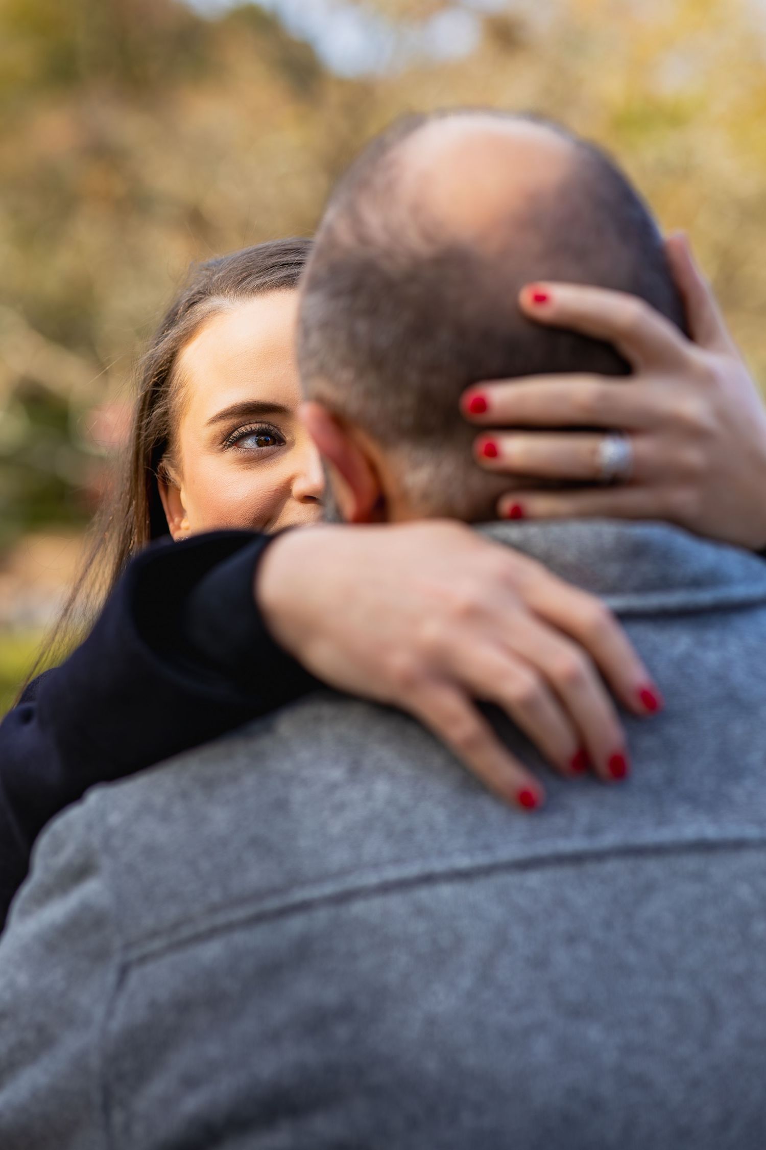 Close-up of hands with red nail polish embracing in an outdoor setting.