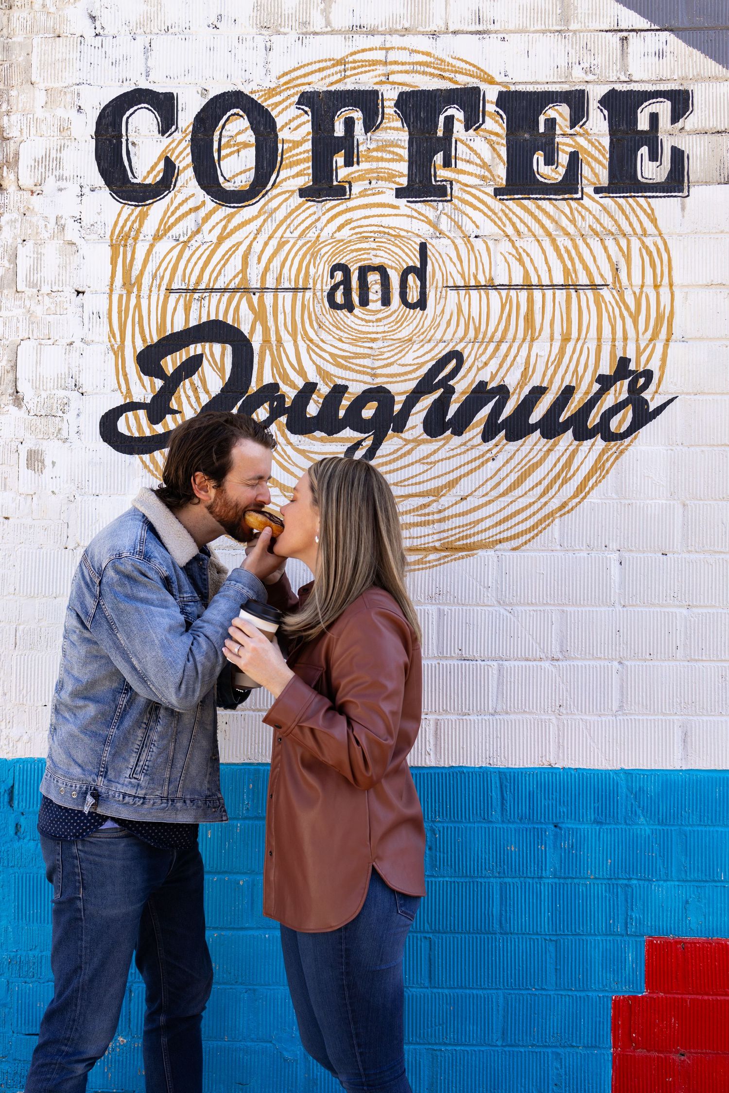 A couple shares intimate moments in front of a coffee shop wall mural.