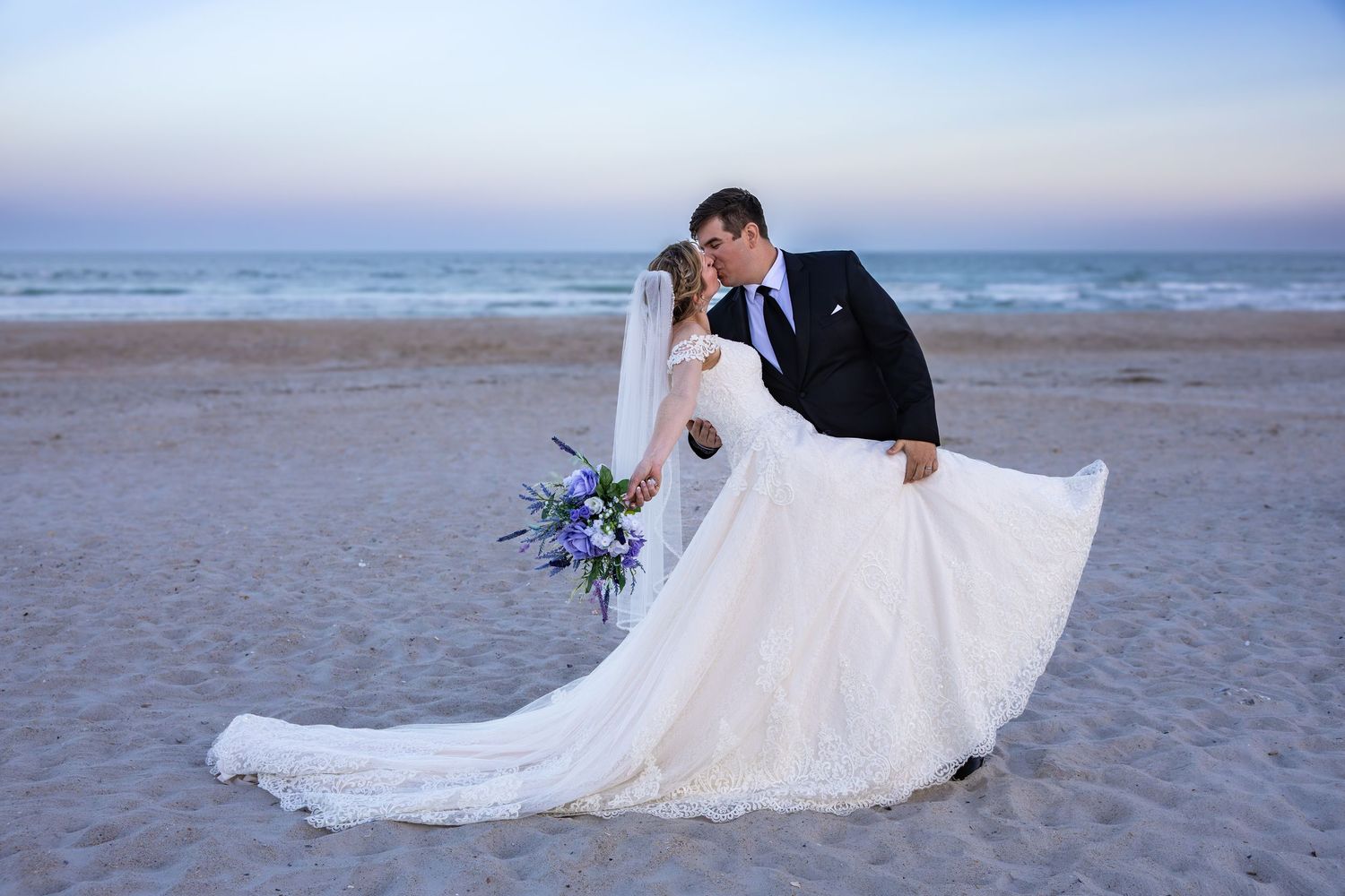 Romantic beach wedding photography session at dusk with flowing white dress.