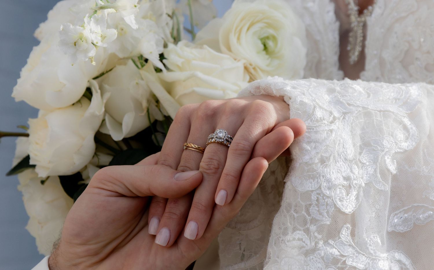 Close-up of hands holding white wedding bouquet against lace dress.