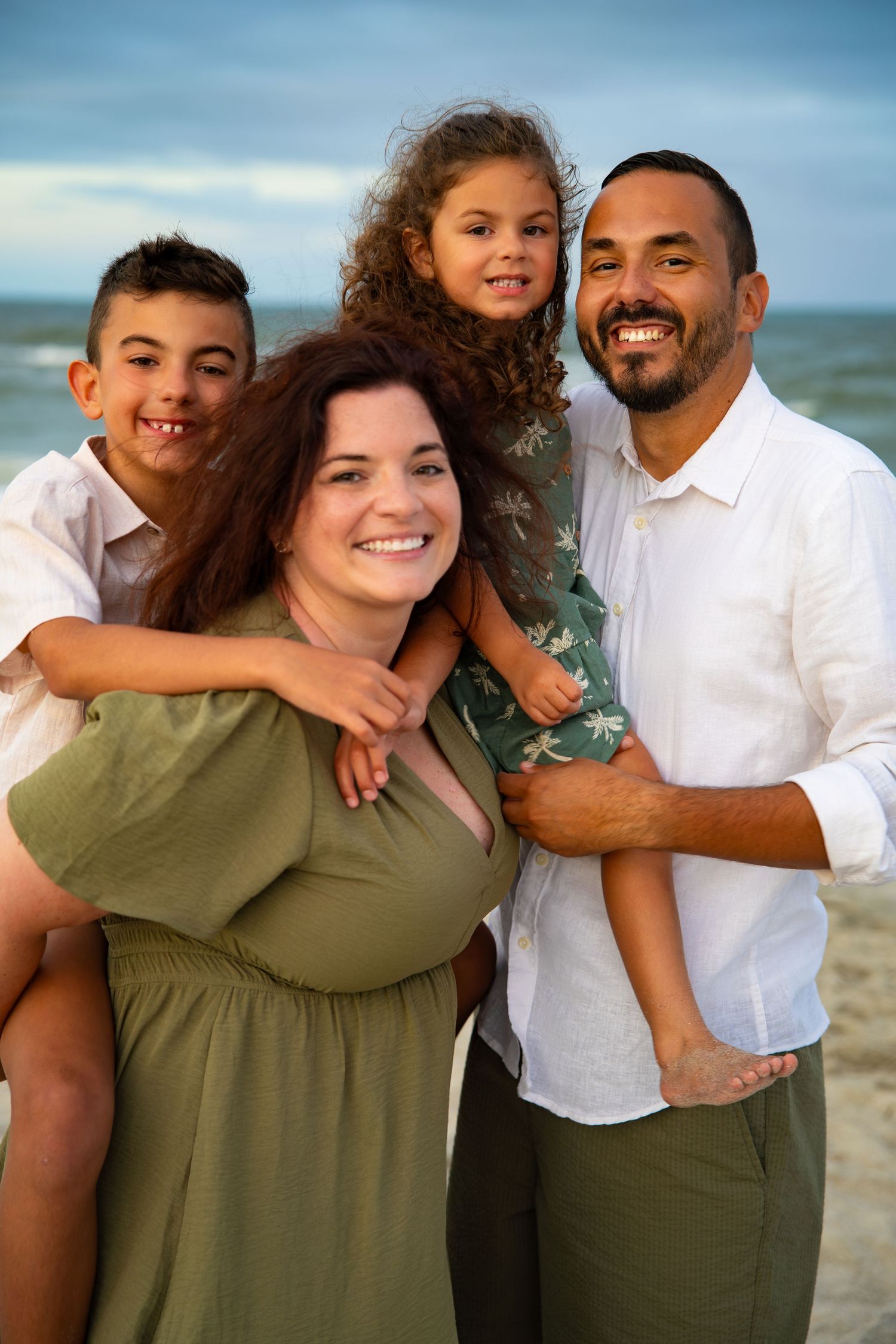 A small group poses together on beach with ocean waves visible in background.