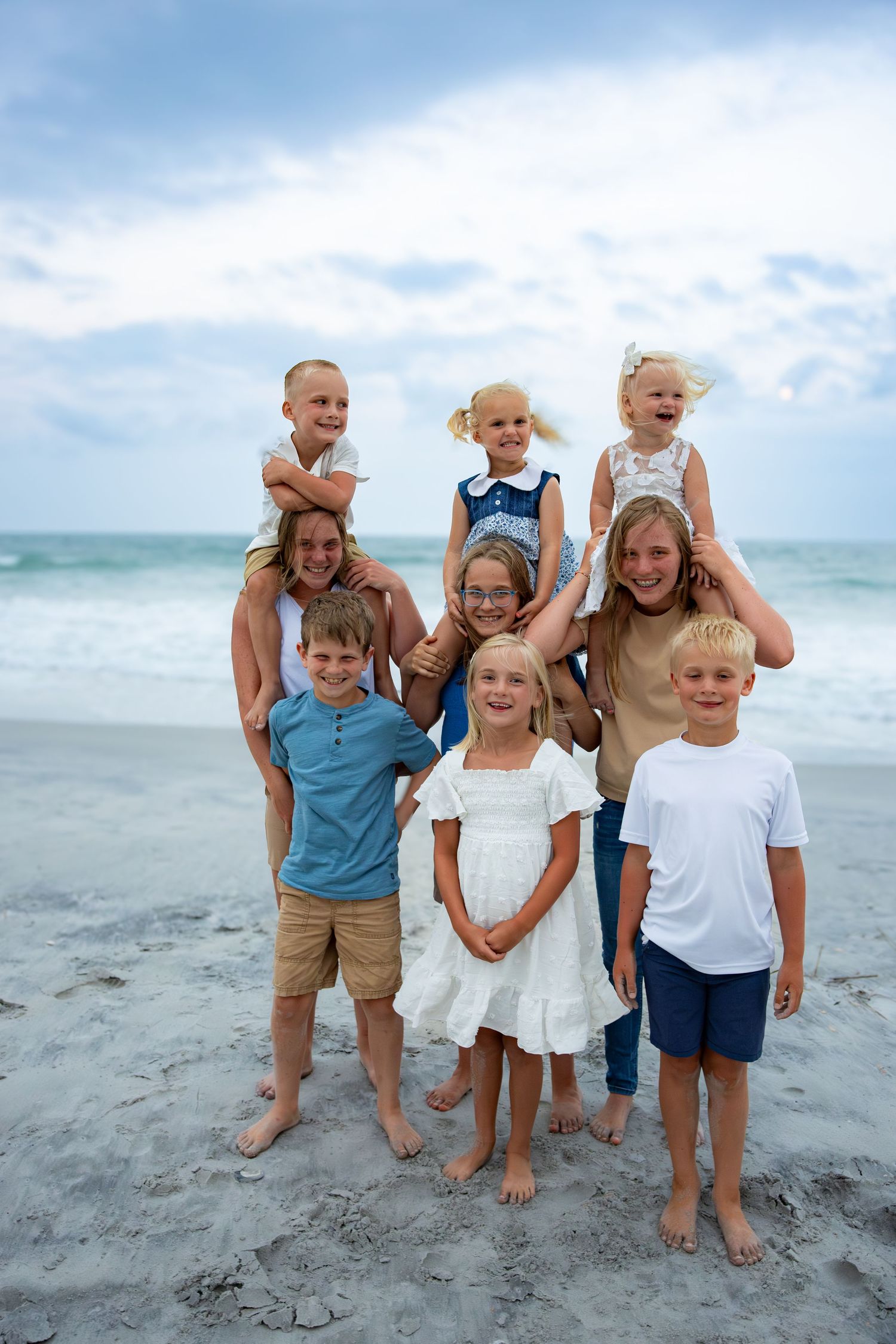 Family group poses together on a sandy beach with ocean waves and blue sky in the background.