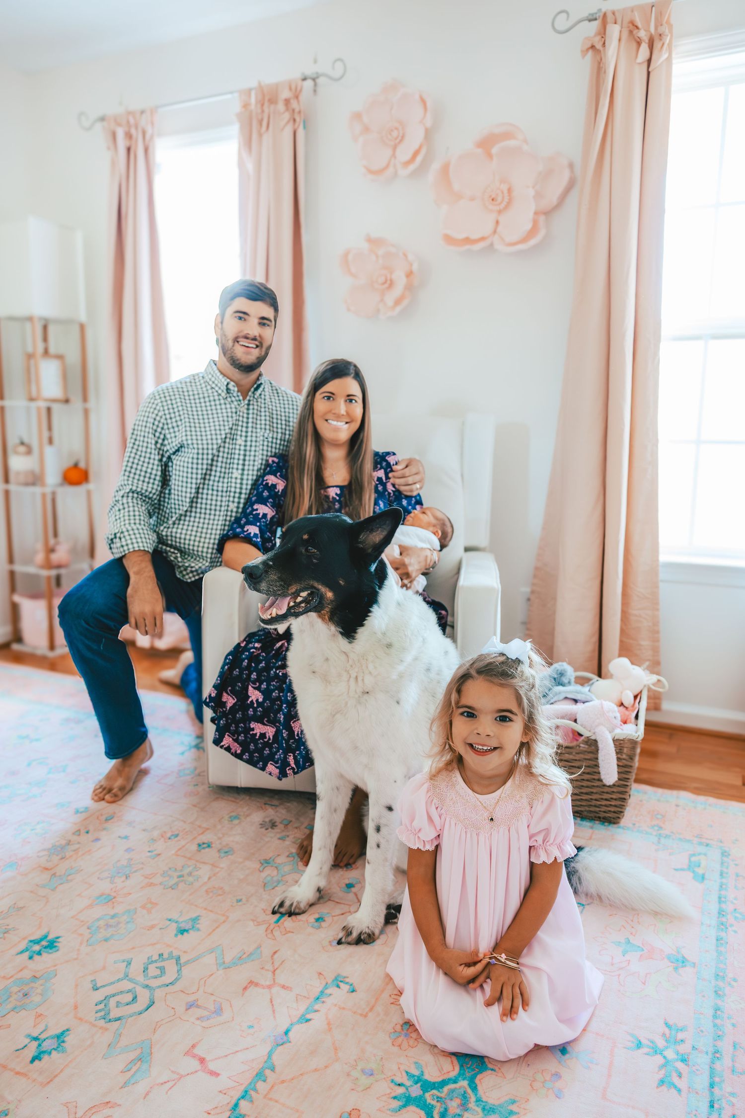 Family photoshoot in pink room with white dog and floral wall decor.