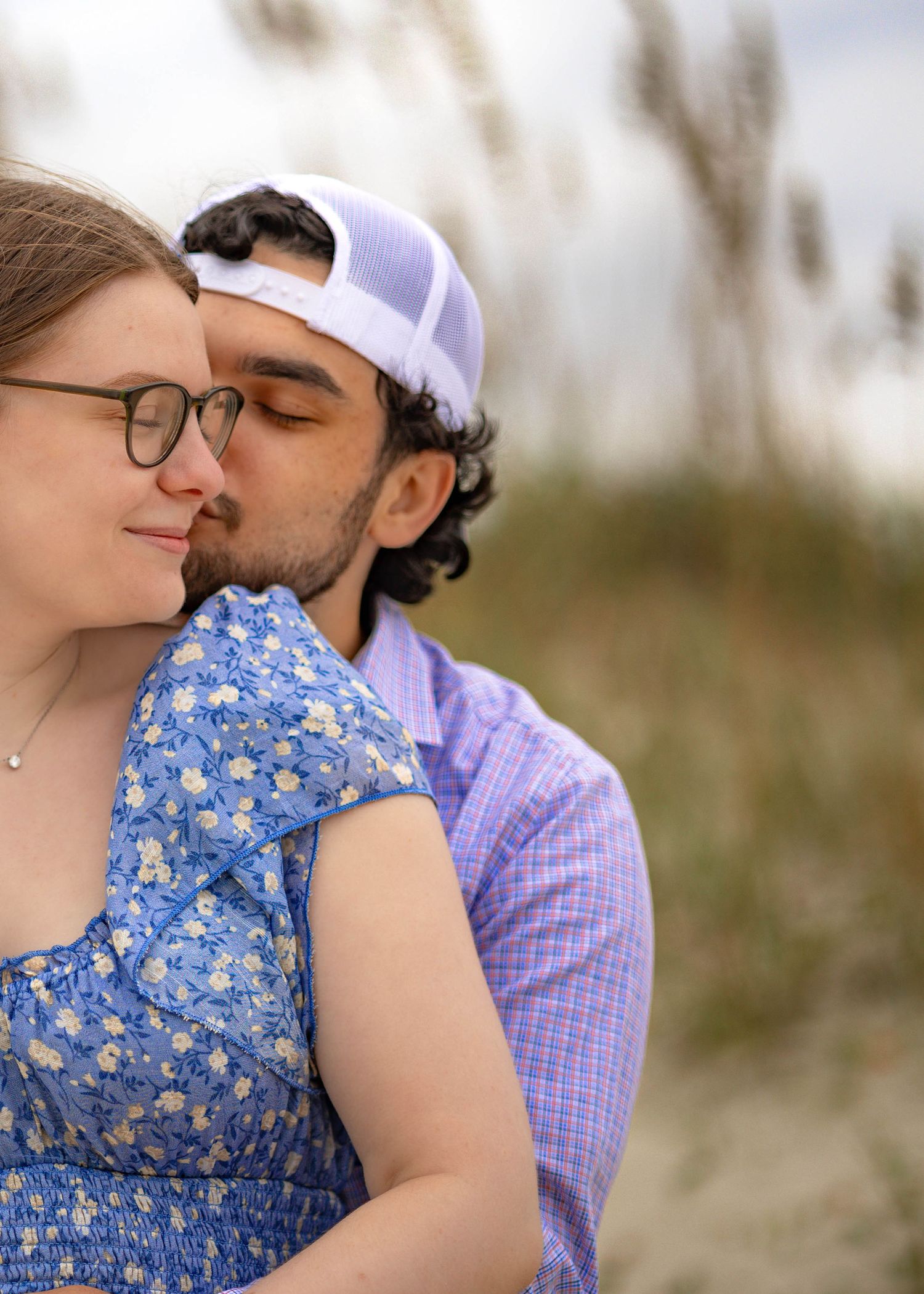 A romantic couple embraces on a beach wearing blue and purple casual attire.