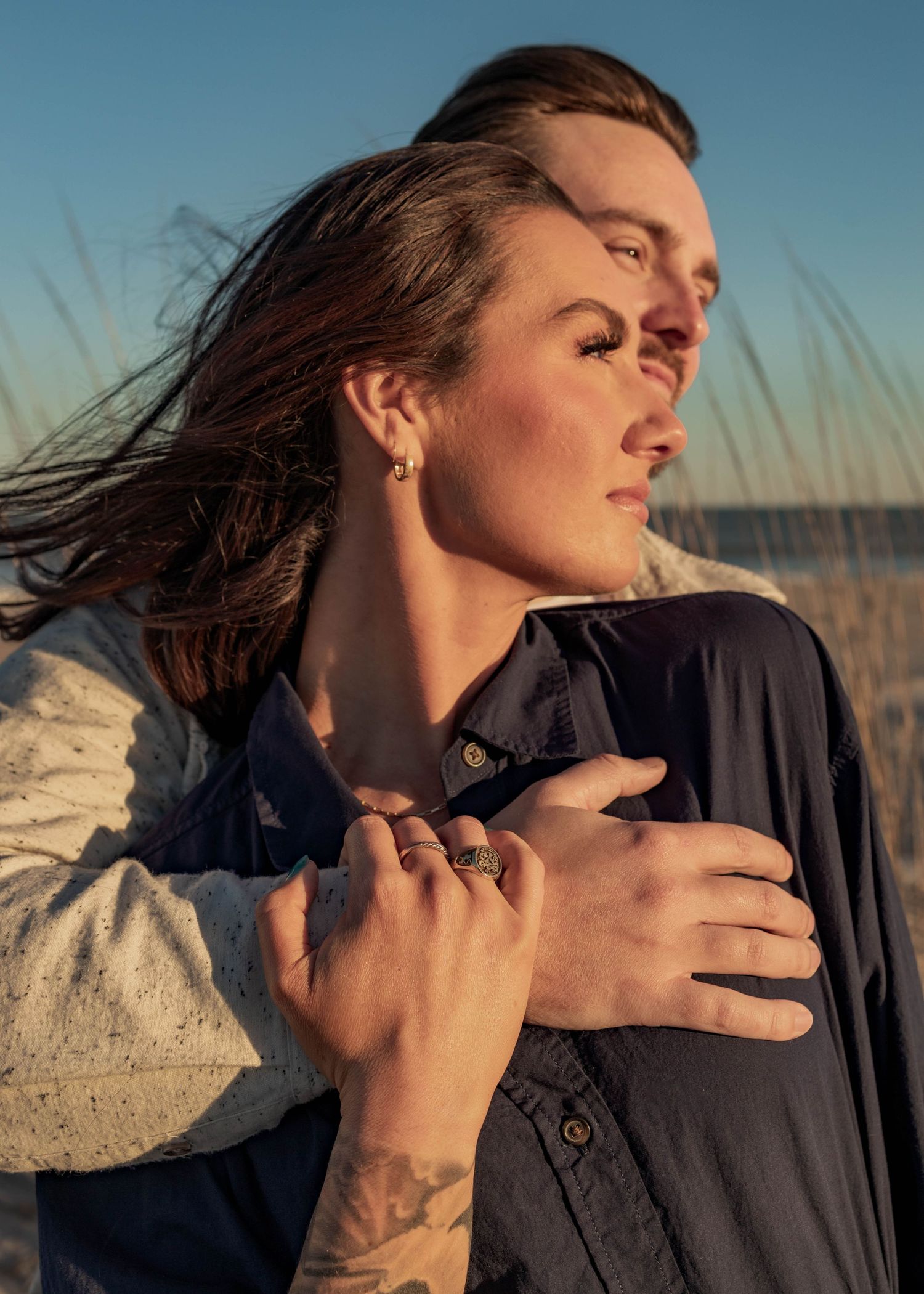 Person in dark clothing poses dramatically against sunset beach backdrop.