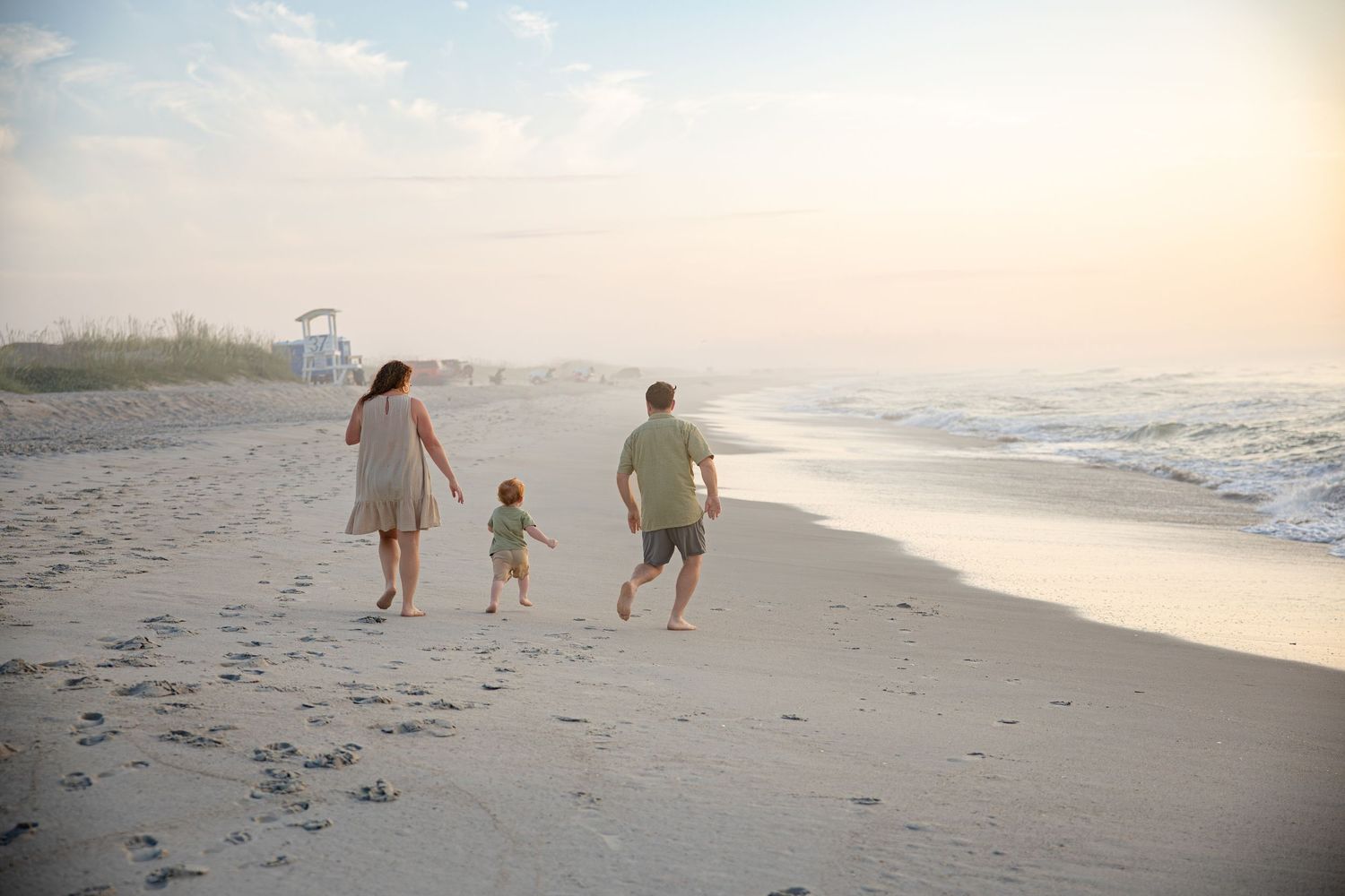 Three figures walk along the shoreline during sunset at the beach.