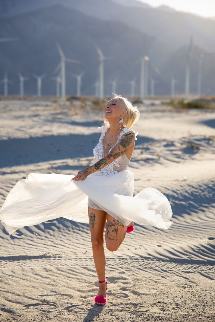White dress flowing in the breeze on a sandy beach during a sunset photoshoot.