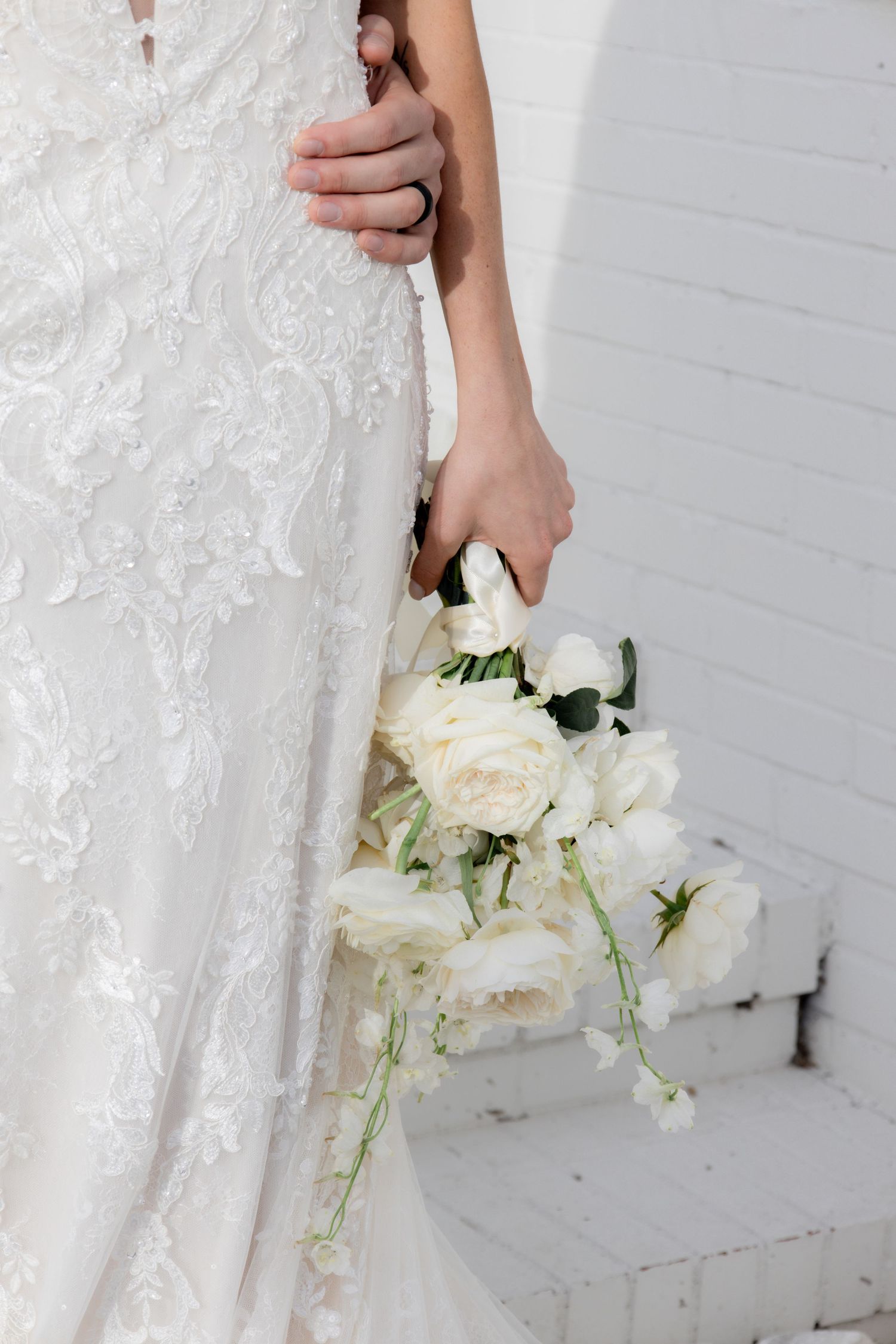 Close-up of white roses bouquet held against lace wedding dress.