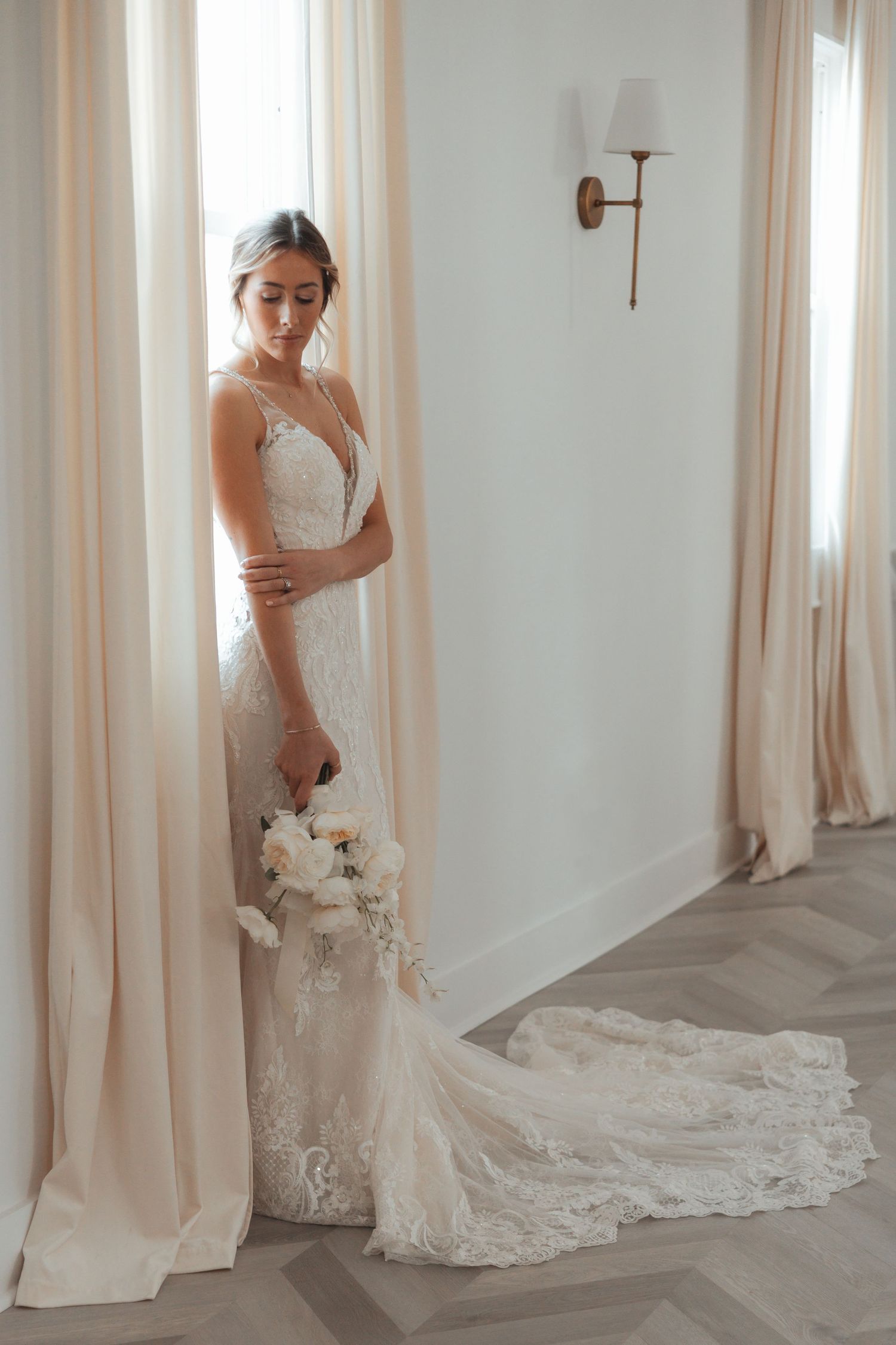Elegant lace wedding dress with long train photographed in bright interior setting.