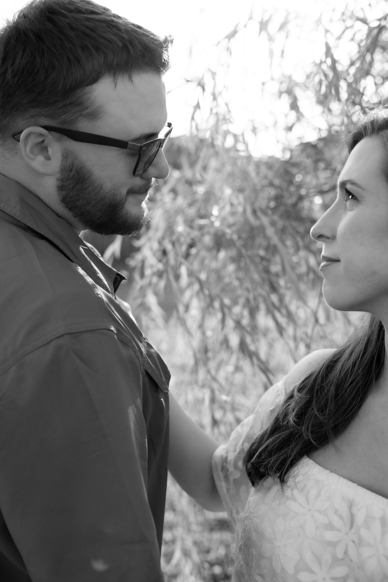 A black and white romantic photo series showing a couple in profile looking at each other against a soft natural background.