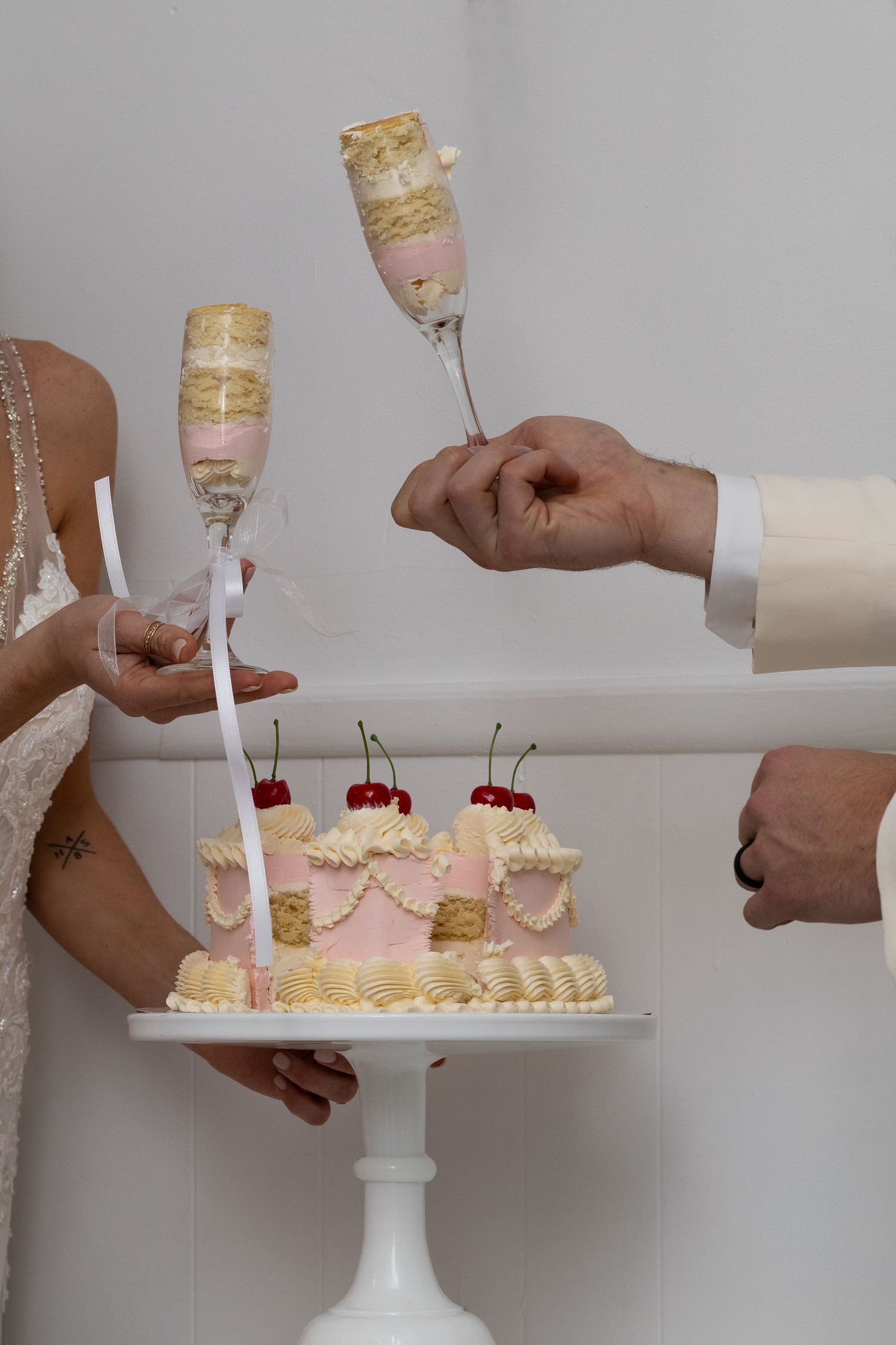 Hands pouring champagne into glasses next to desserts on white cake stand.