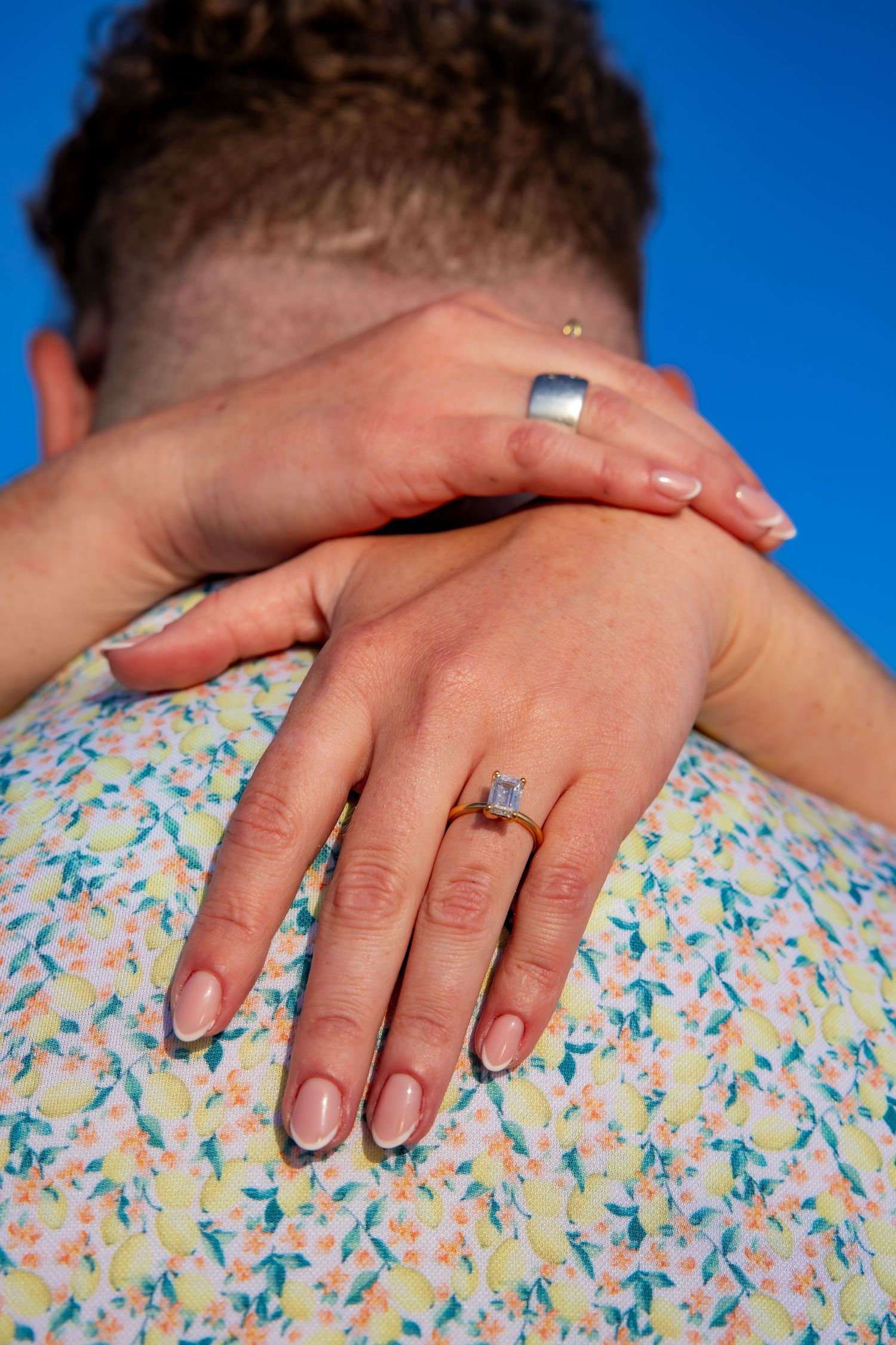 Close up of hands showing matching silver rings against blue background.