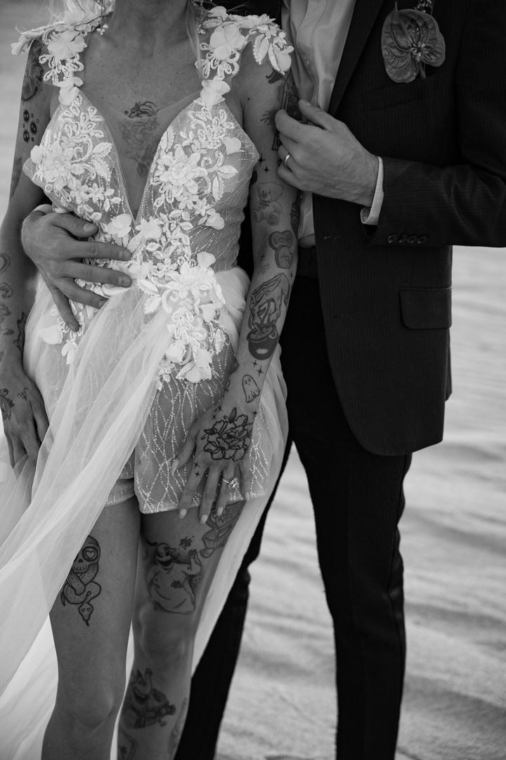 Black and white photo of tattooed bride in lace wedding dress with groom in dark suit.