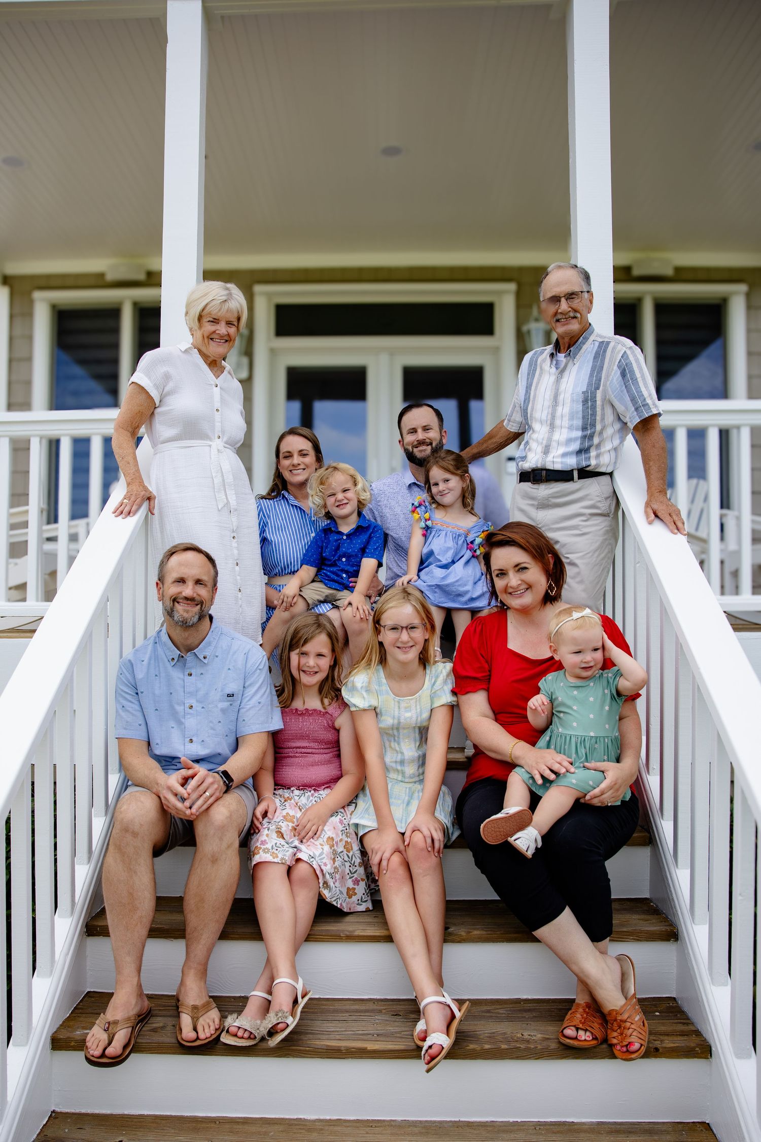 Multi-generational family poses together on white porch steps of a beach house.