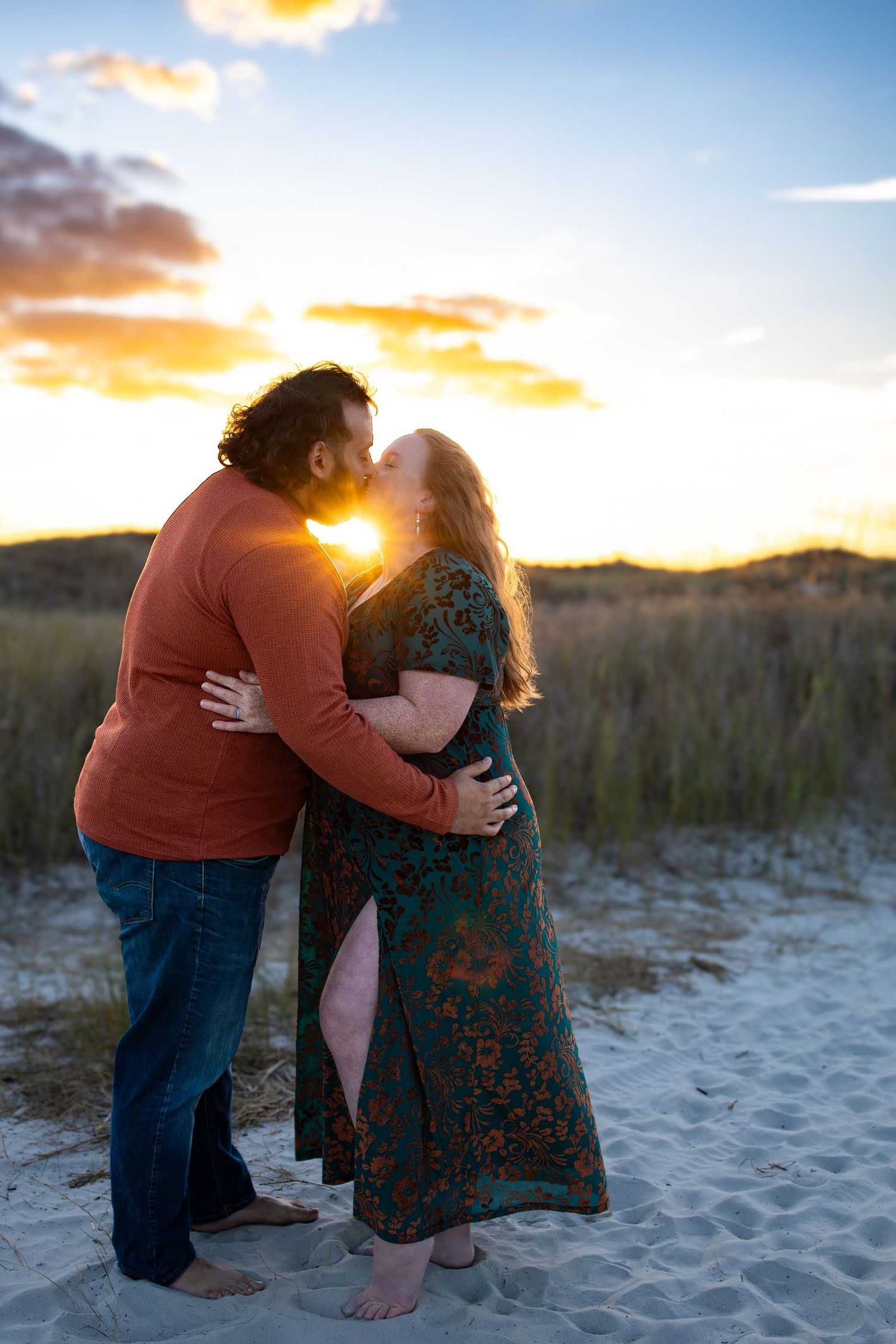 Sunset beach photoshoot capturing intimate moments between couple on sandy dunes.