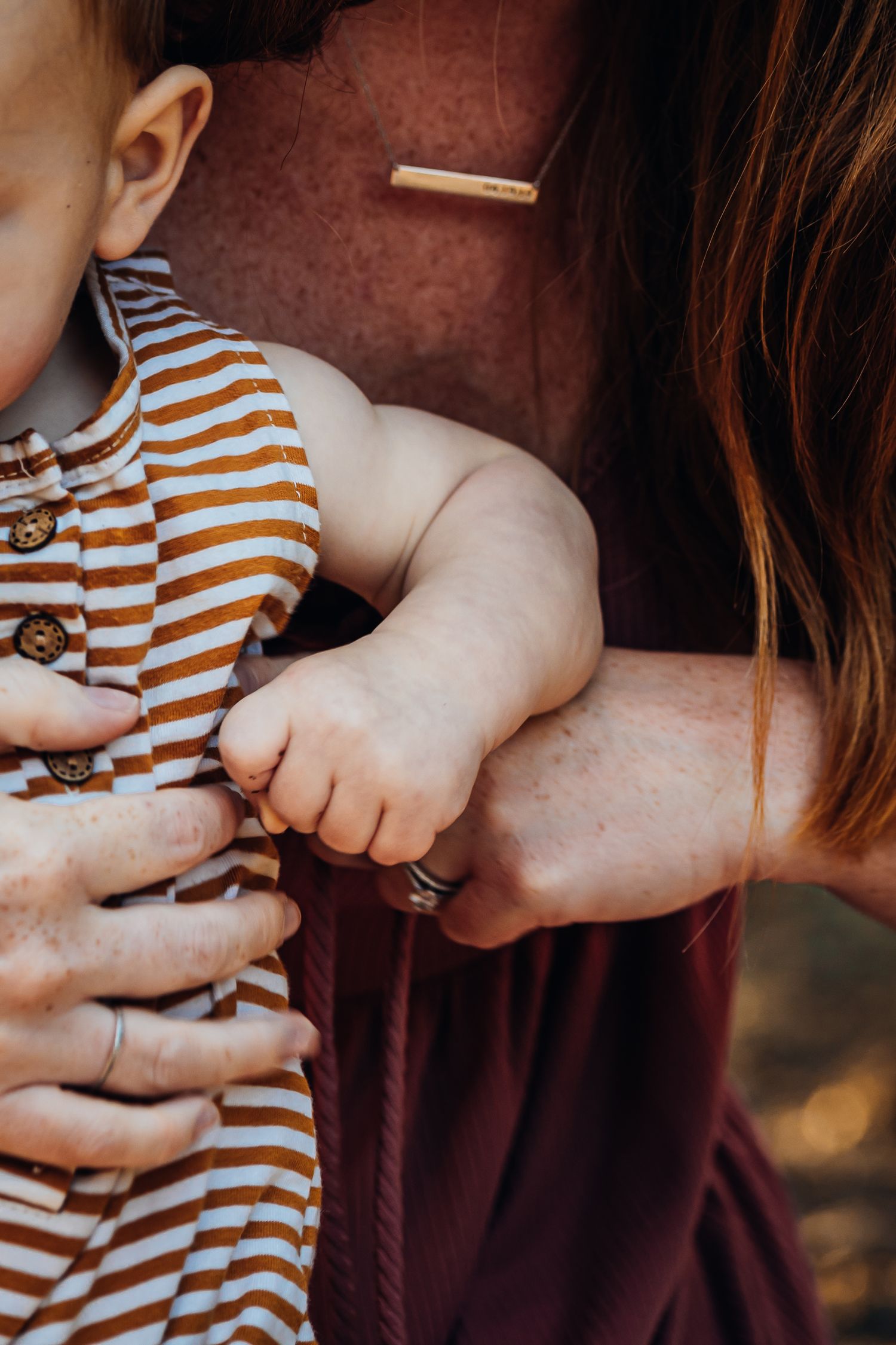 Close-up of hands holding small baby in striped clothing.