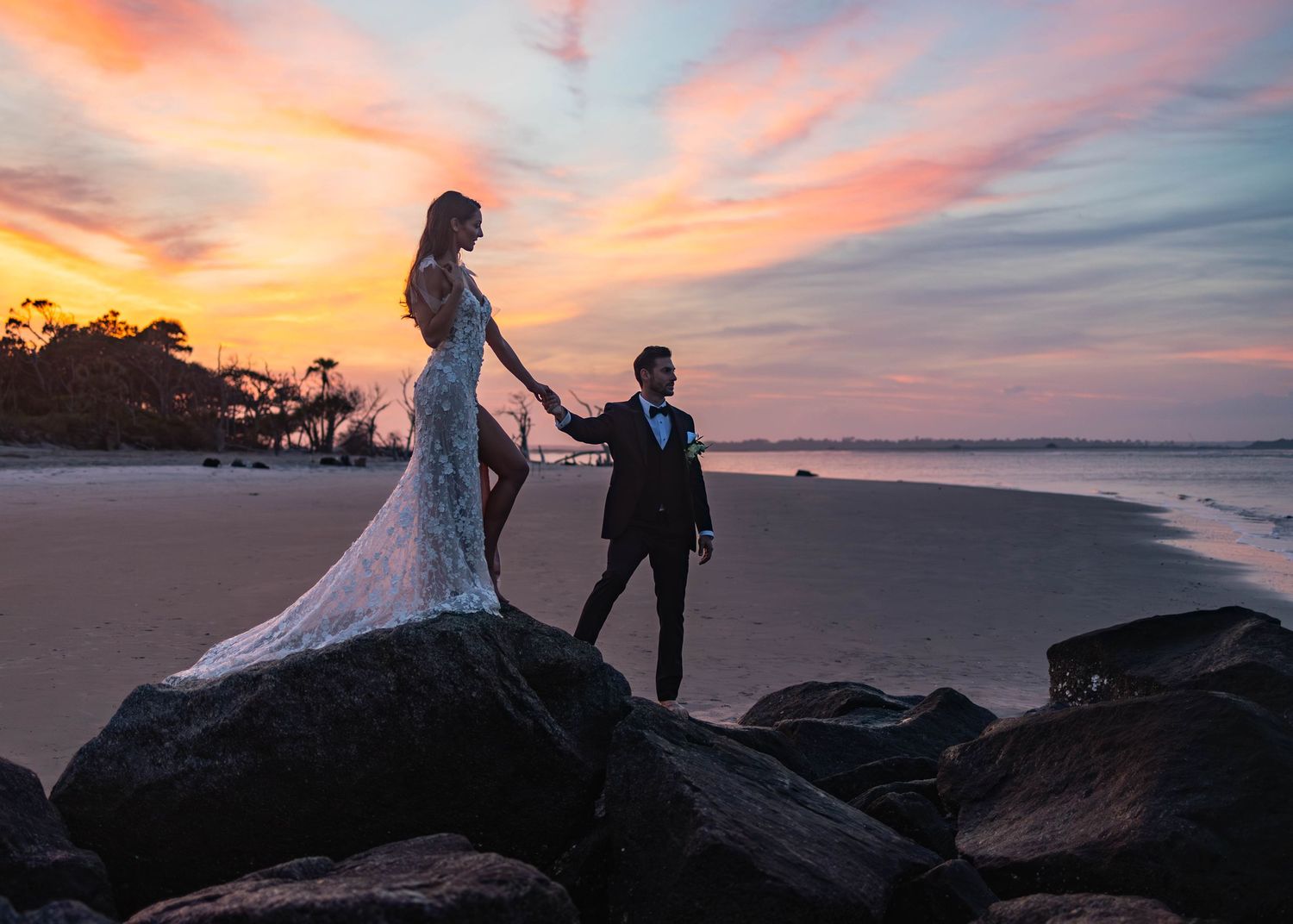 Dramatic sunset sky over rocky coastline with silhouetted figures.