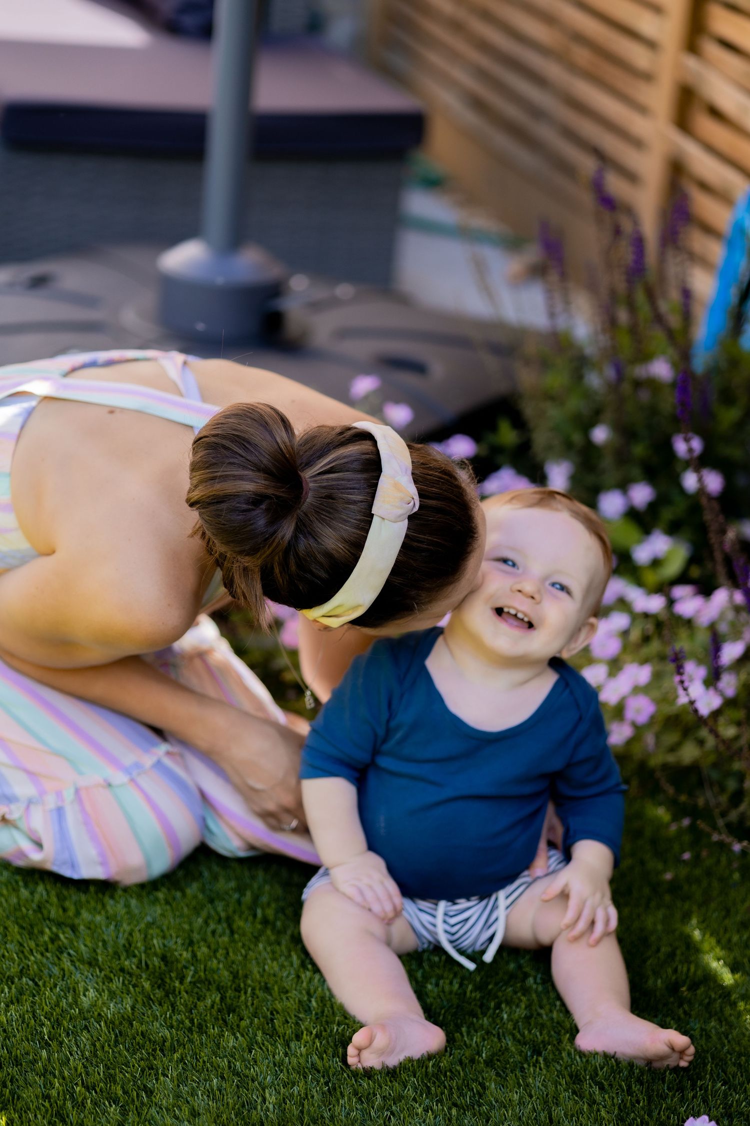 Baby in navy outfit playing on grass near purple flowers.