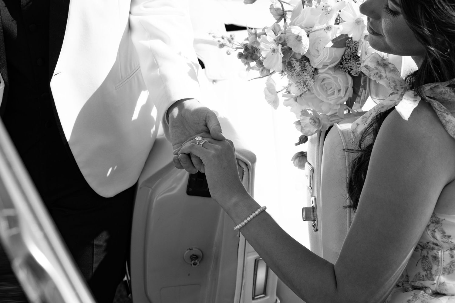 Black and white wedding photo of bride pinning boutonniere on groom while holding floral bouquet.