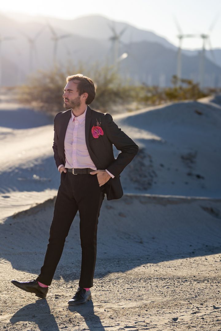 Person in formal suit poses dramatically against desert mountain backdrop.