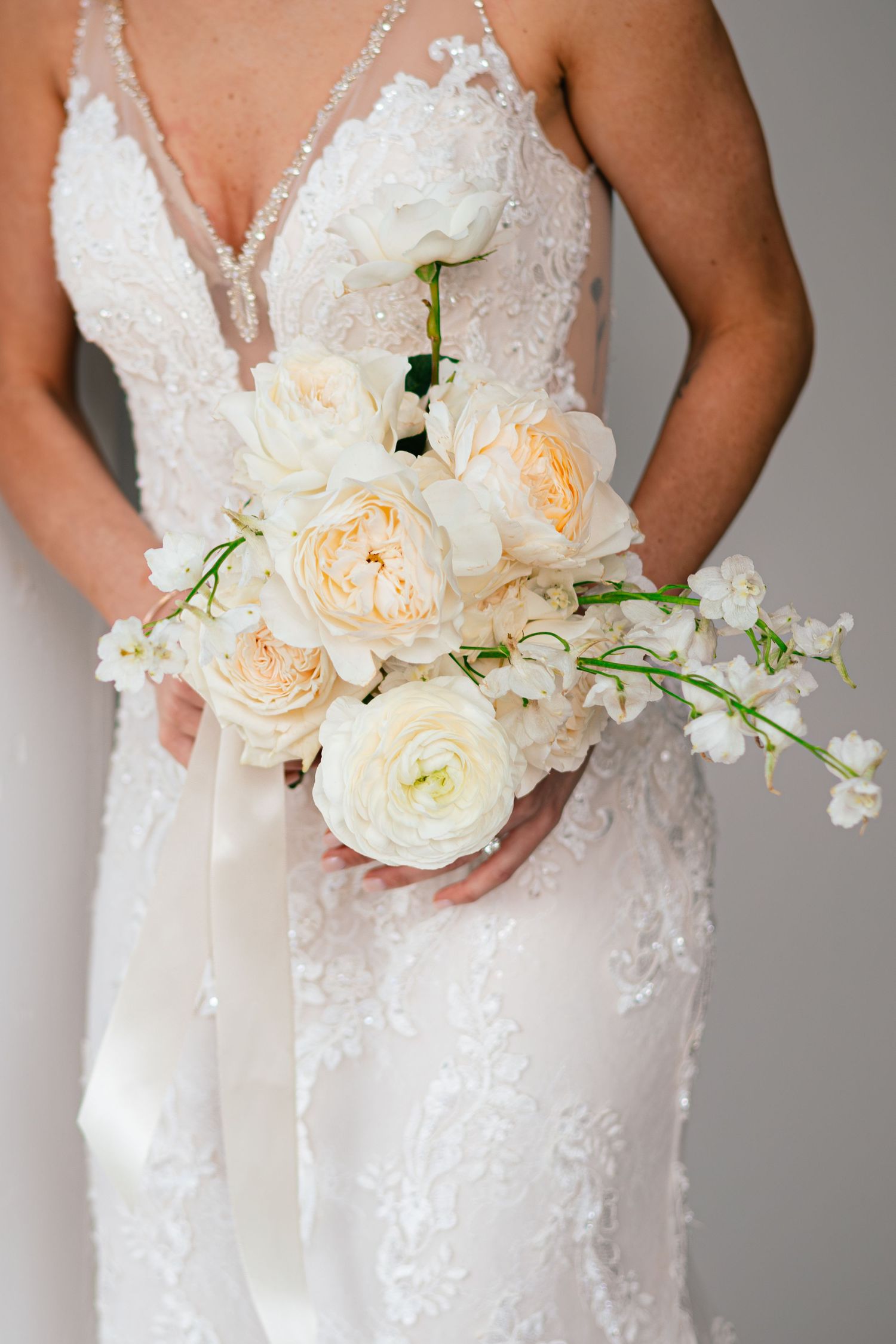 Bride holding delicate bouquet of white and peach roses against lace wedding dress.