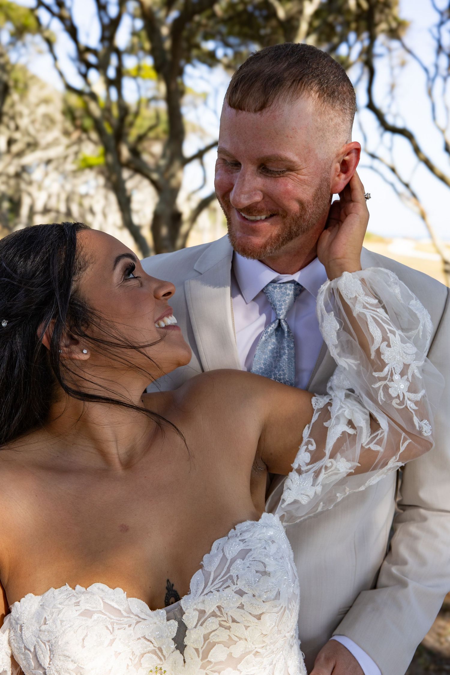 Wedding couple shares intimate moments under trees in natural outdoor lighting.