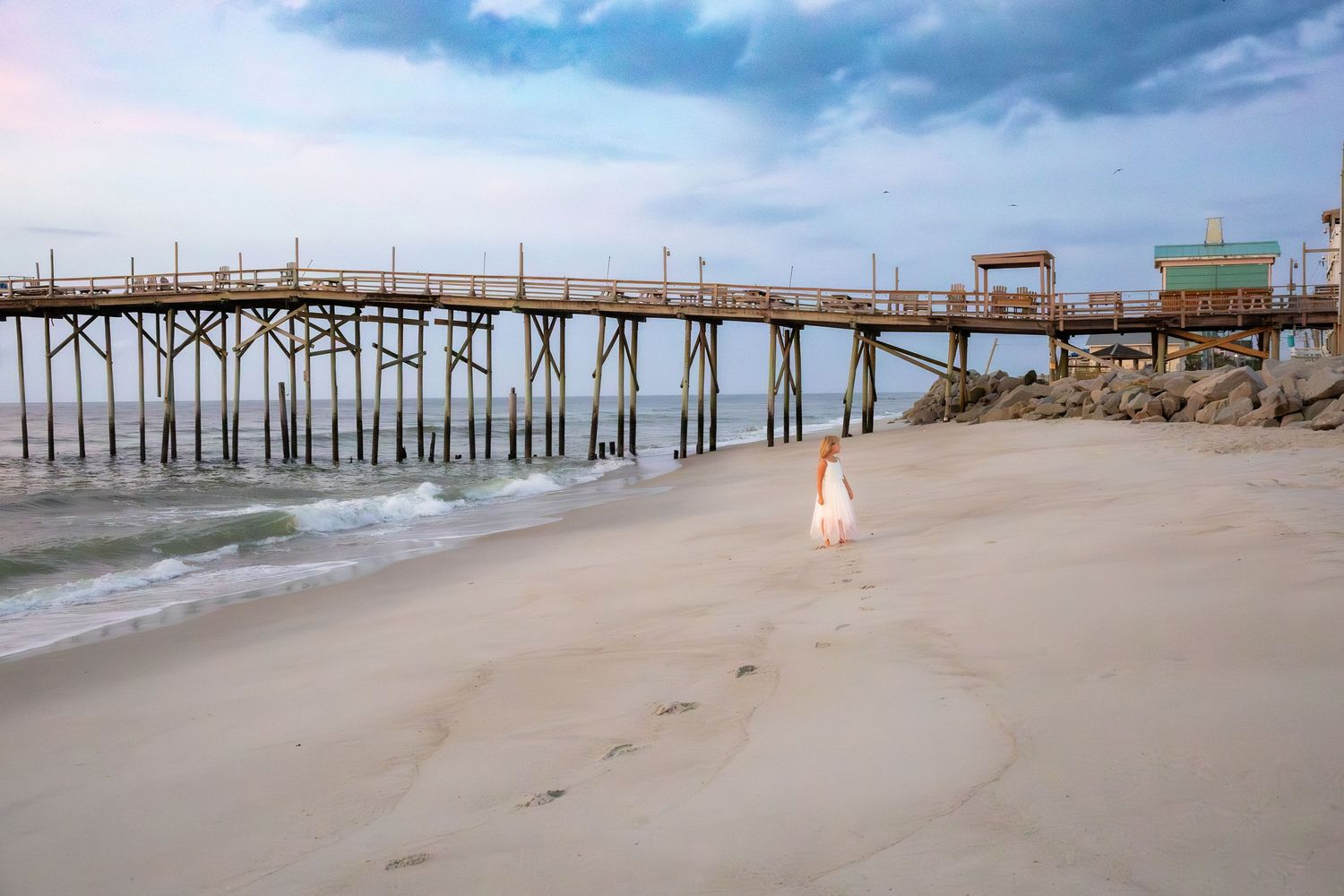 Dreamy beach scene with wooden pier and soft pastel sky at sunset.