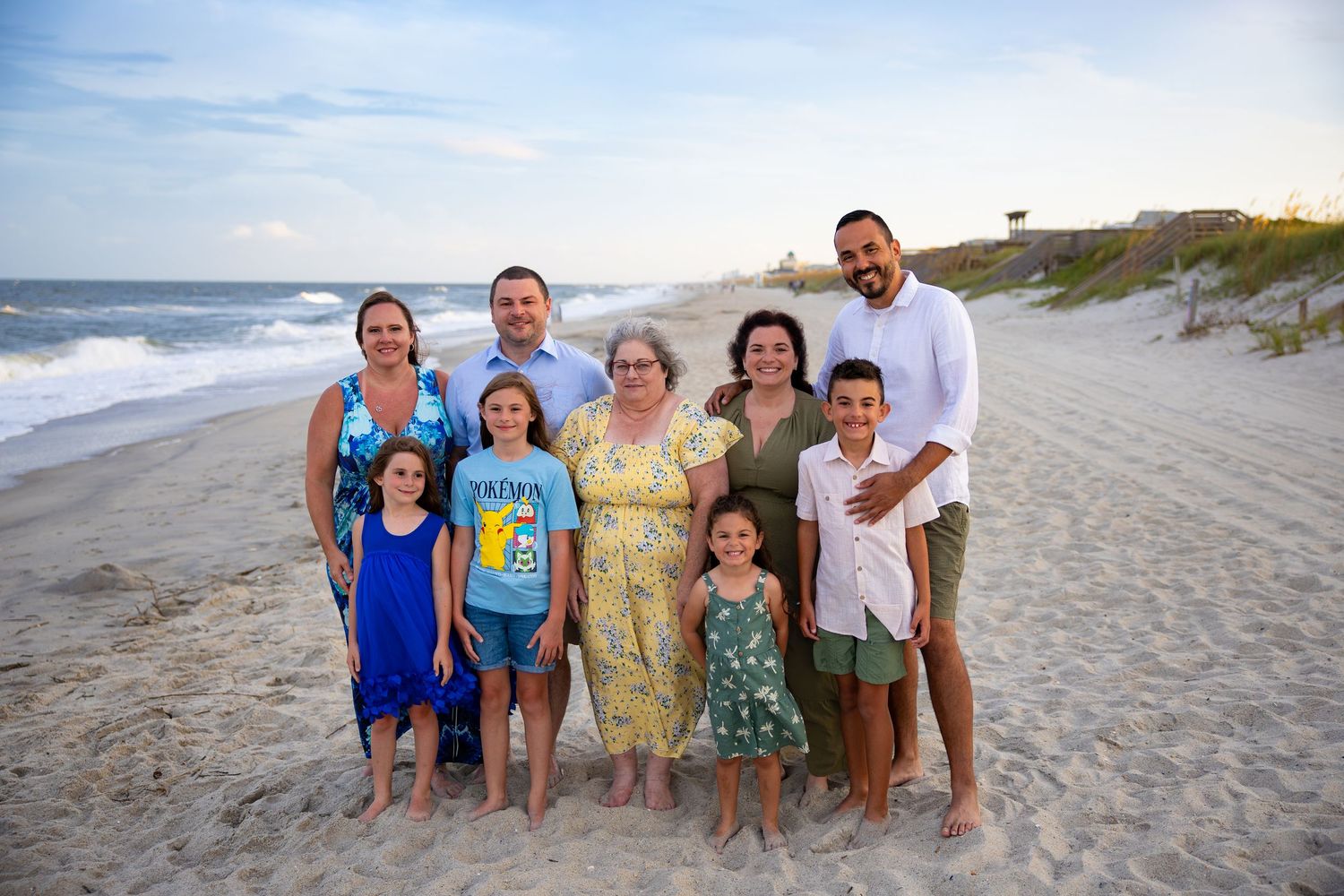 A group poses together on sandy beach with ocean waves and blue sky in background.