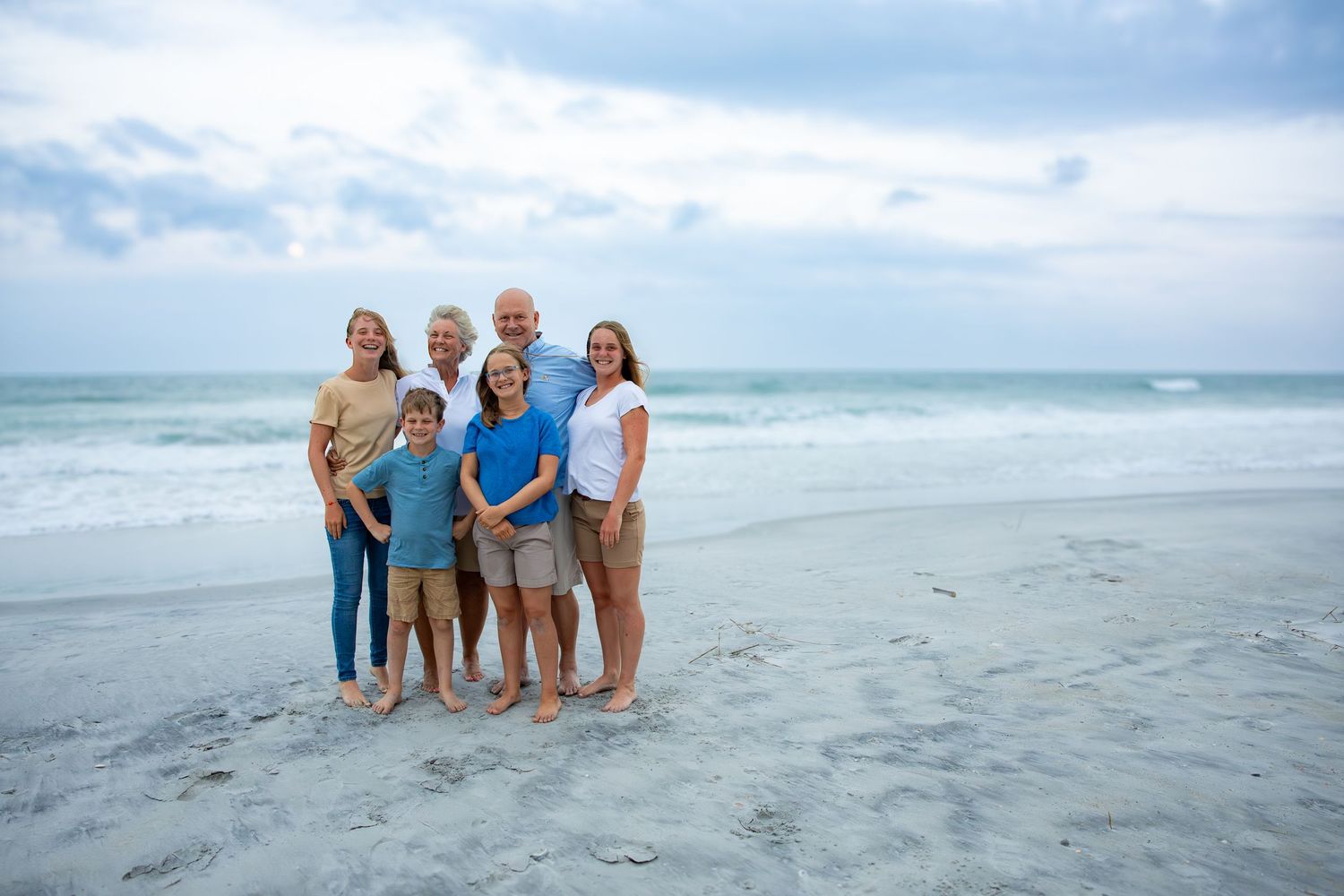 Small group stands together on beach with ocean waves rolling in behind them.