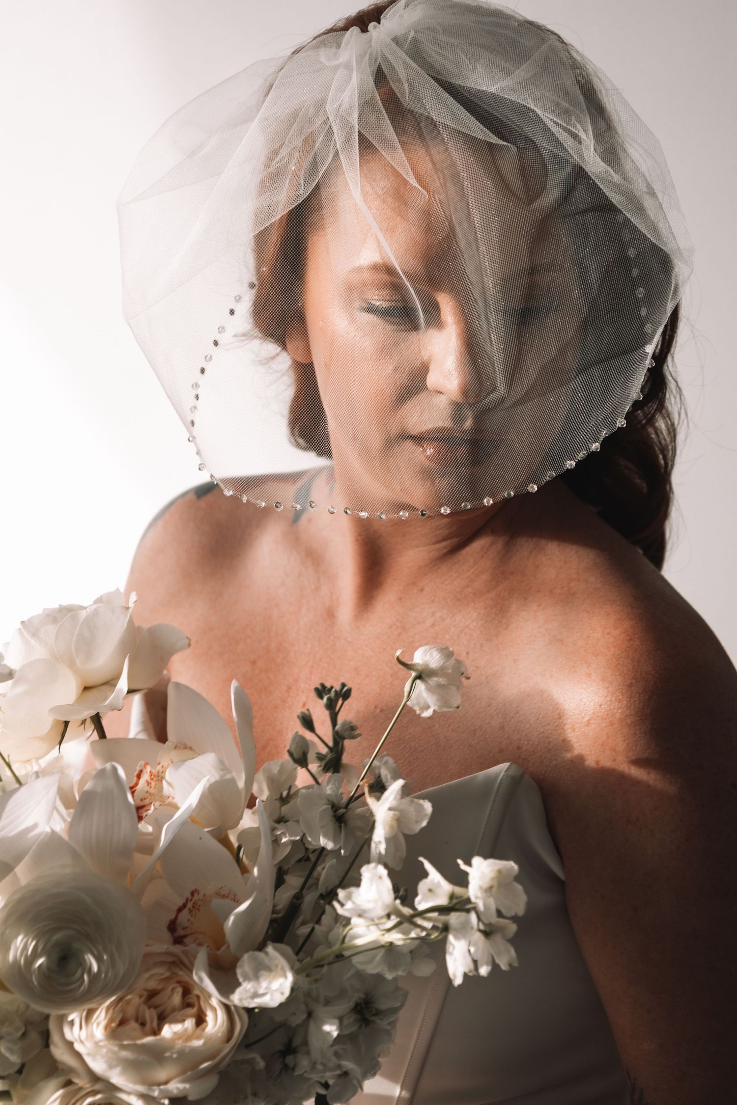 Artistic bridal portrait with white flowers and veil in soft lighting.
