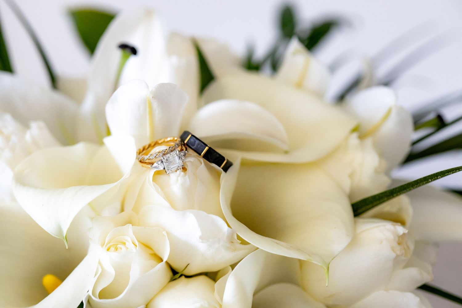 Gold and black wedding rings resting on a white calla lily bridal bouquet.