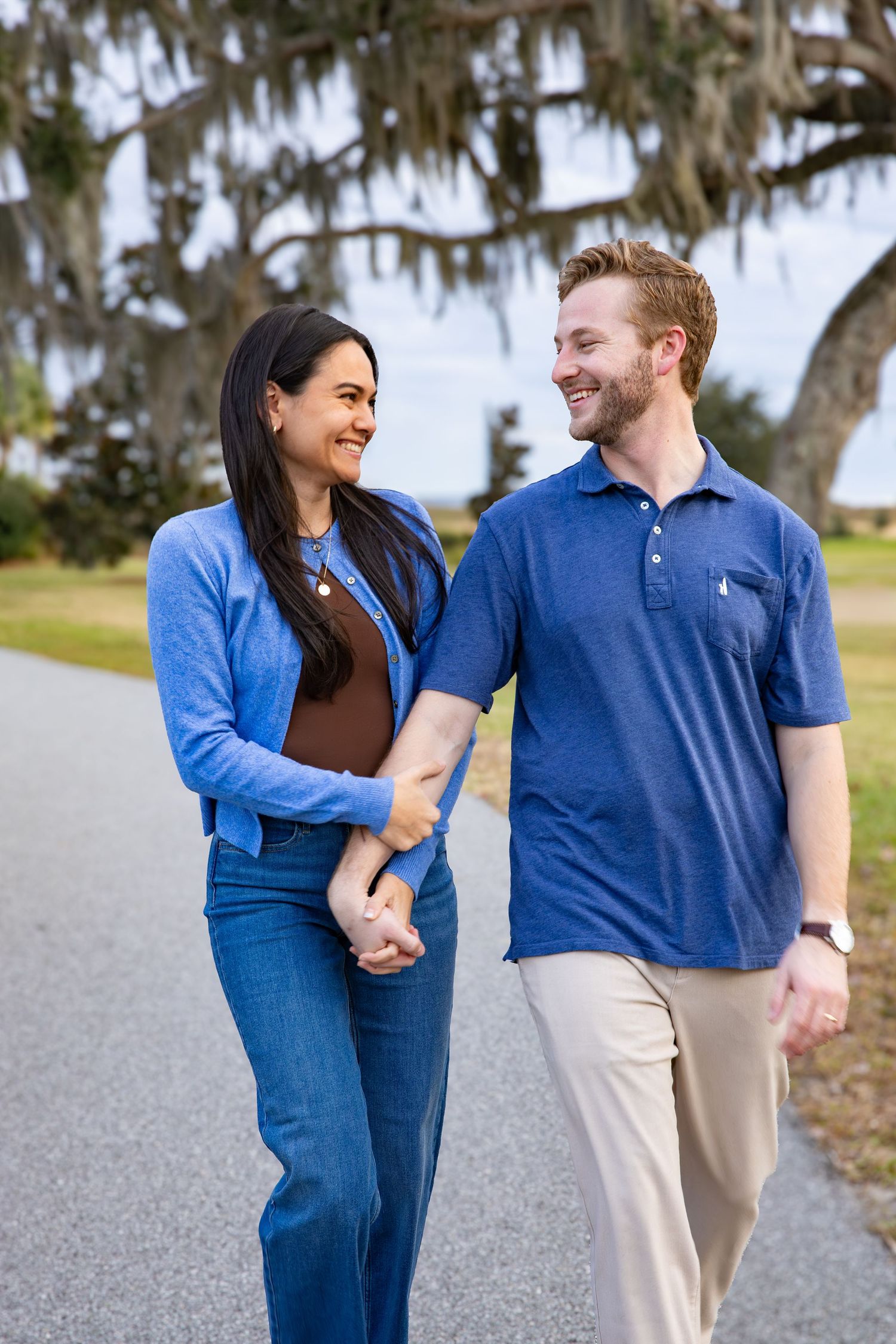 Couple in matching blue outfits walking and laughing together on gravel path.