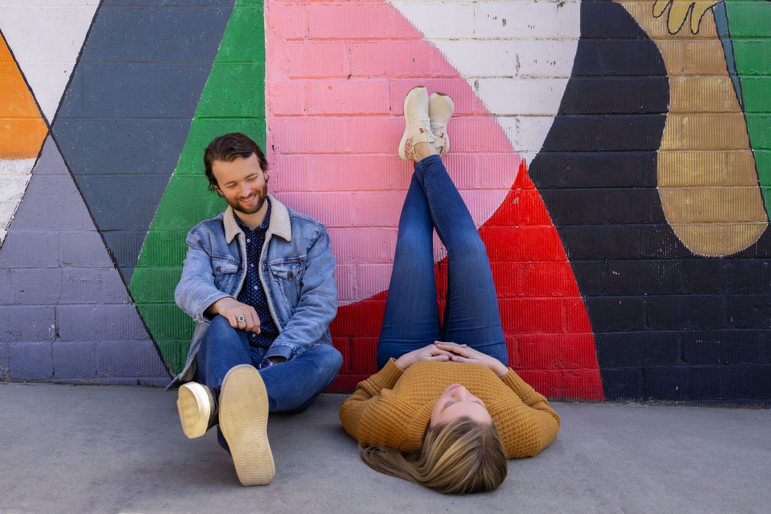 A couple poses playfully against a colorful painted wall mural.