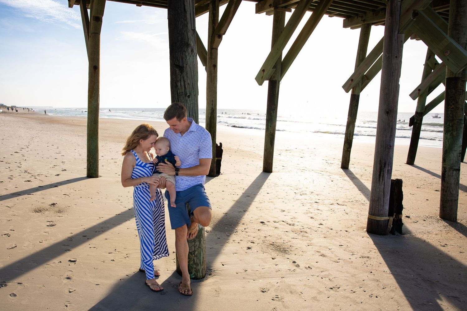 Couple shares a tender moment under a beach pier during golden hour.