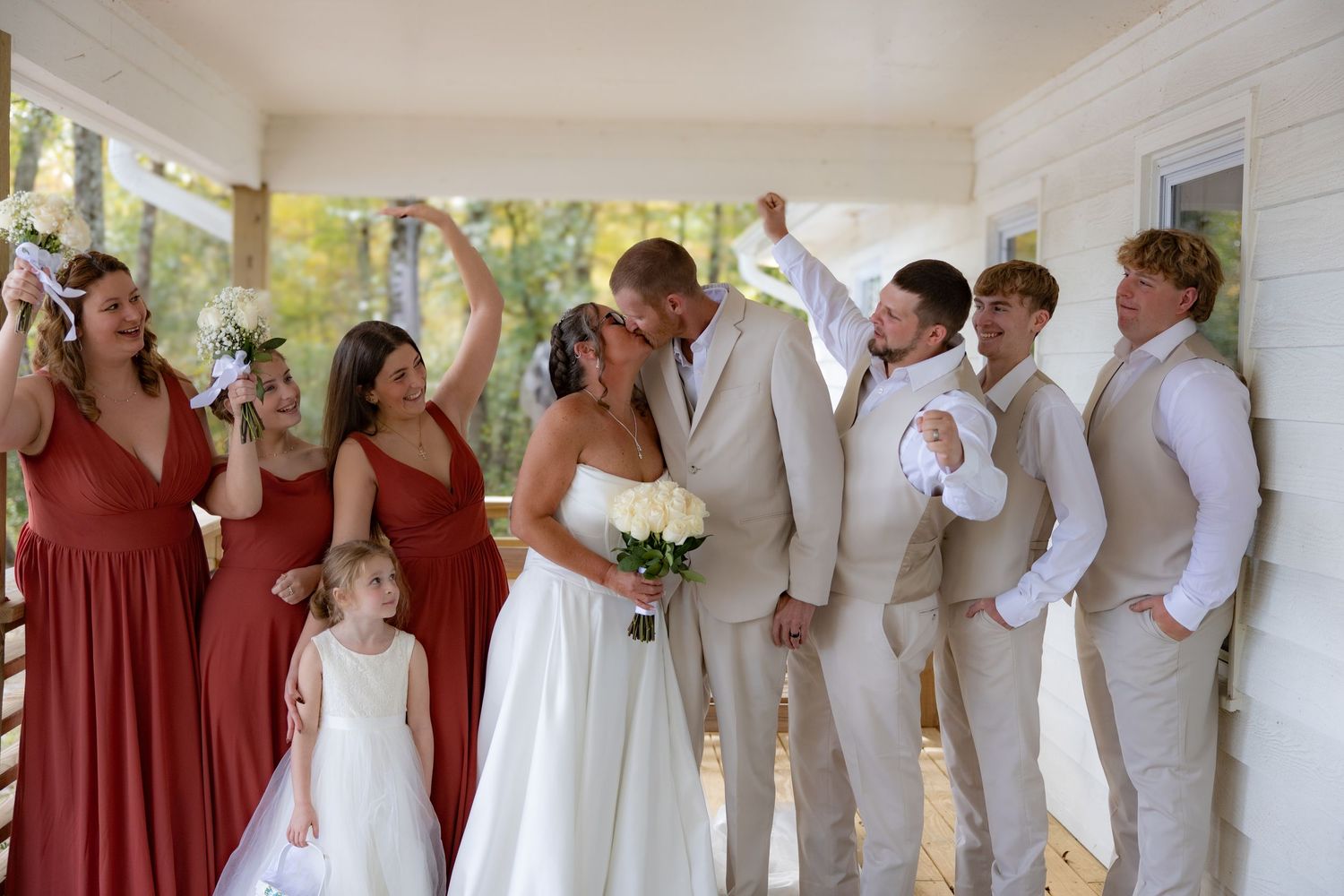 Wedding party in white and burgundy attire posing together on a porch.