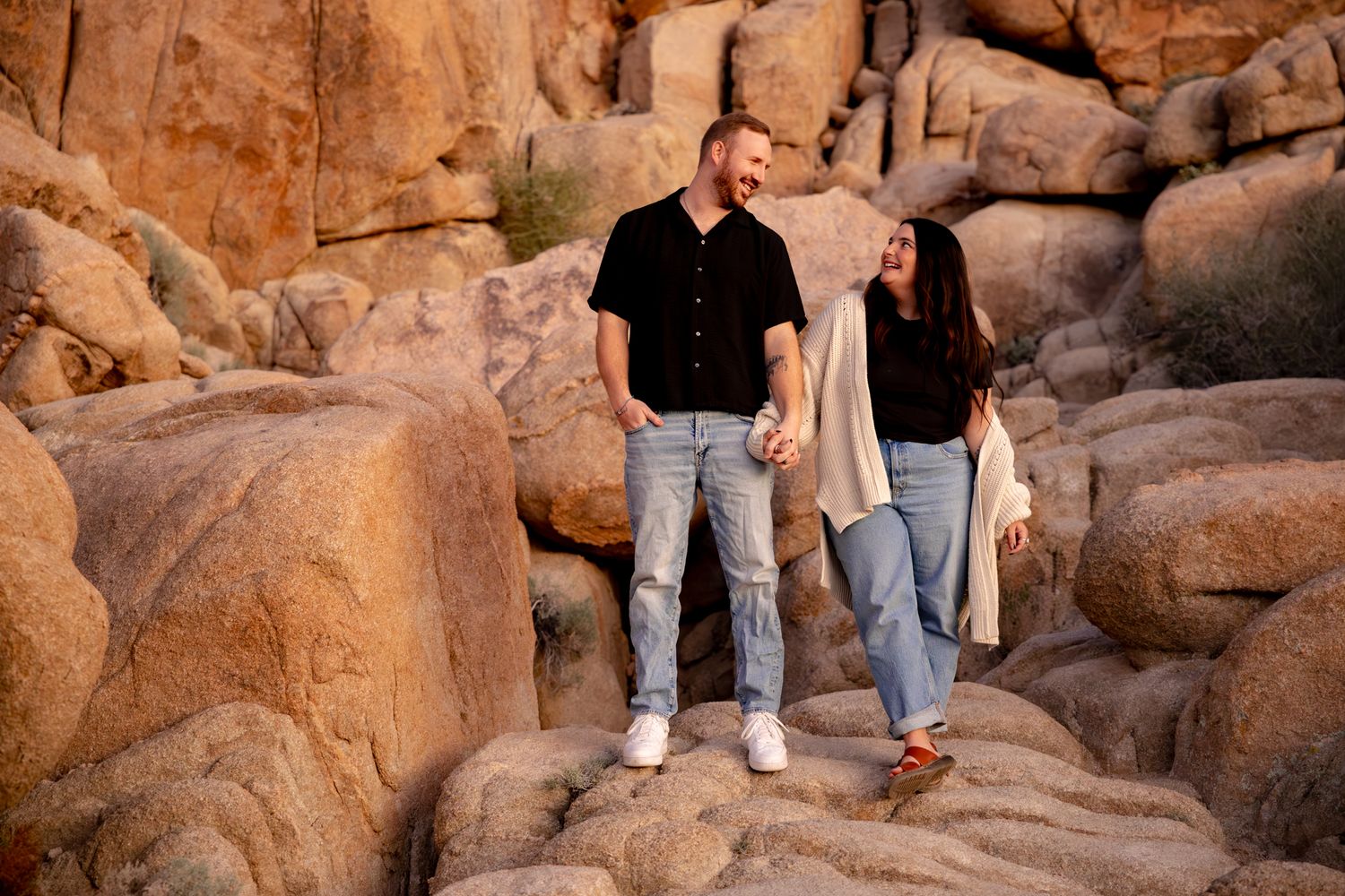 A couple stands together on large desert boulders during golden hour at Joshua Tree National Park.