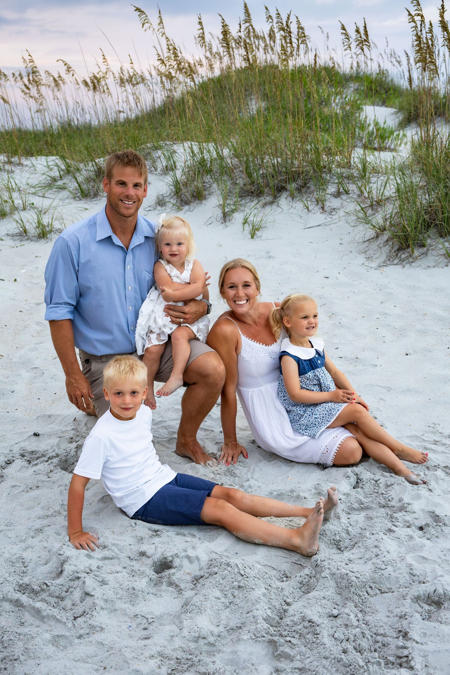 A group poses together on sandy dunes with sea oats in background at sunset.