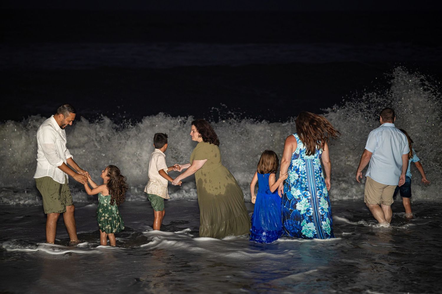 A group plays in ocean waves at night with water splashing around them.