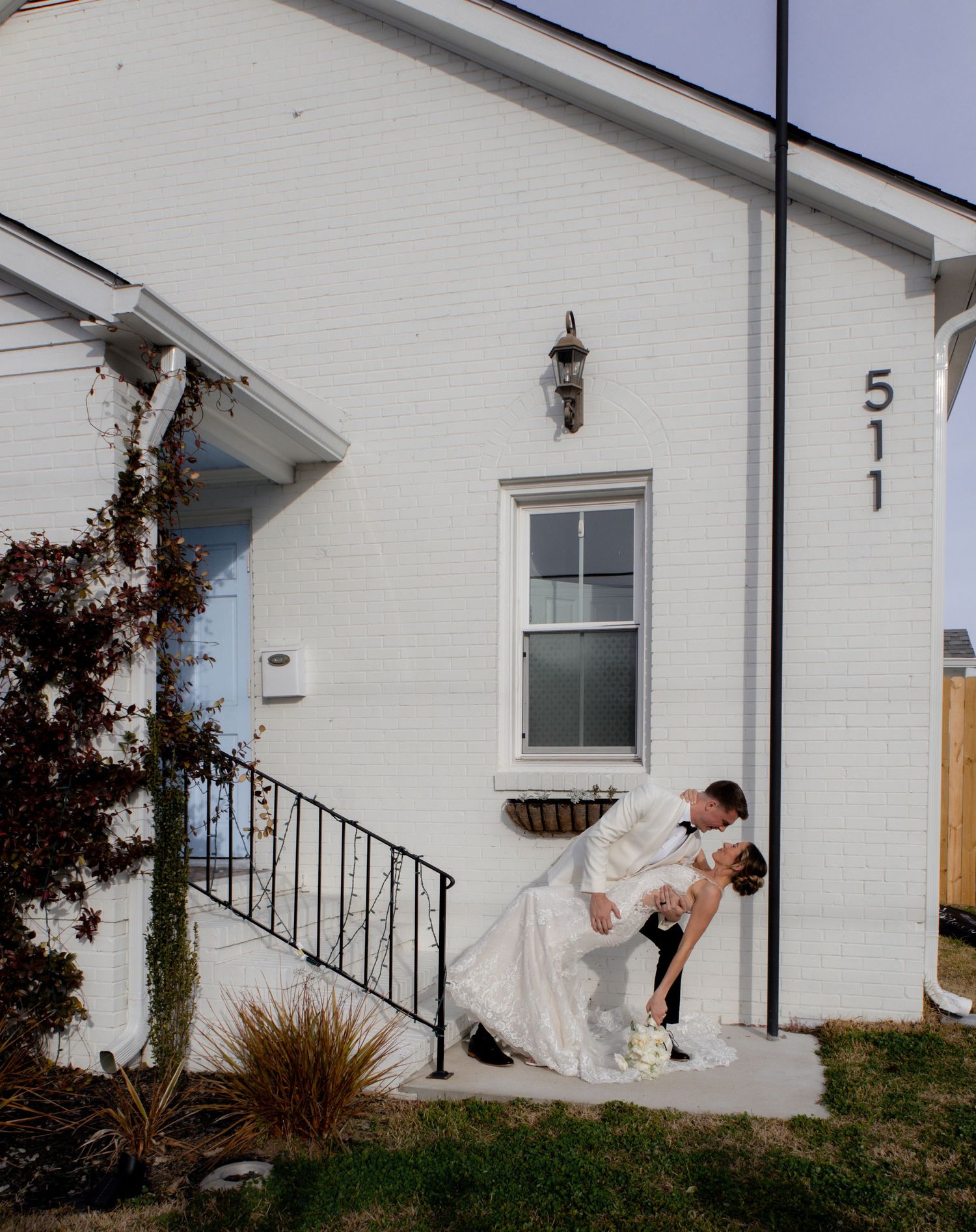 Playful wedding photos taken outside a white brick house with iron railings.