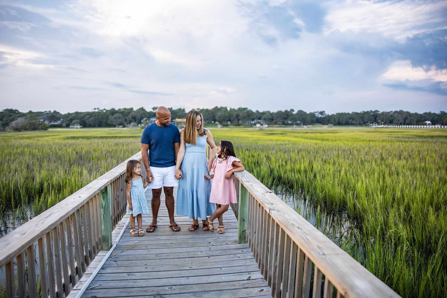 A group stands together on a wooden boardwalk surrounded by tall marsh grass on a sunny day.