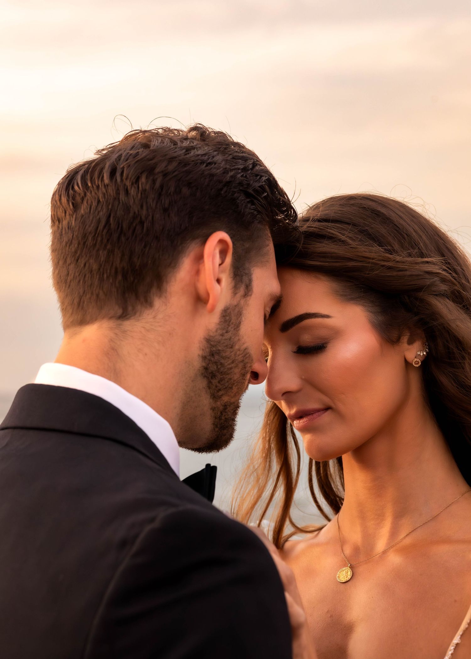 Intimate sunset portrait of couple in formal attire by the ocean.