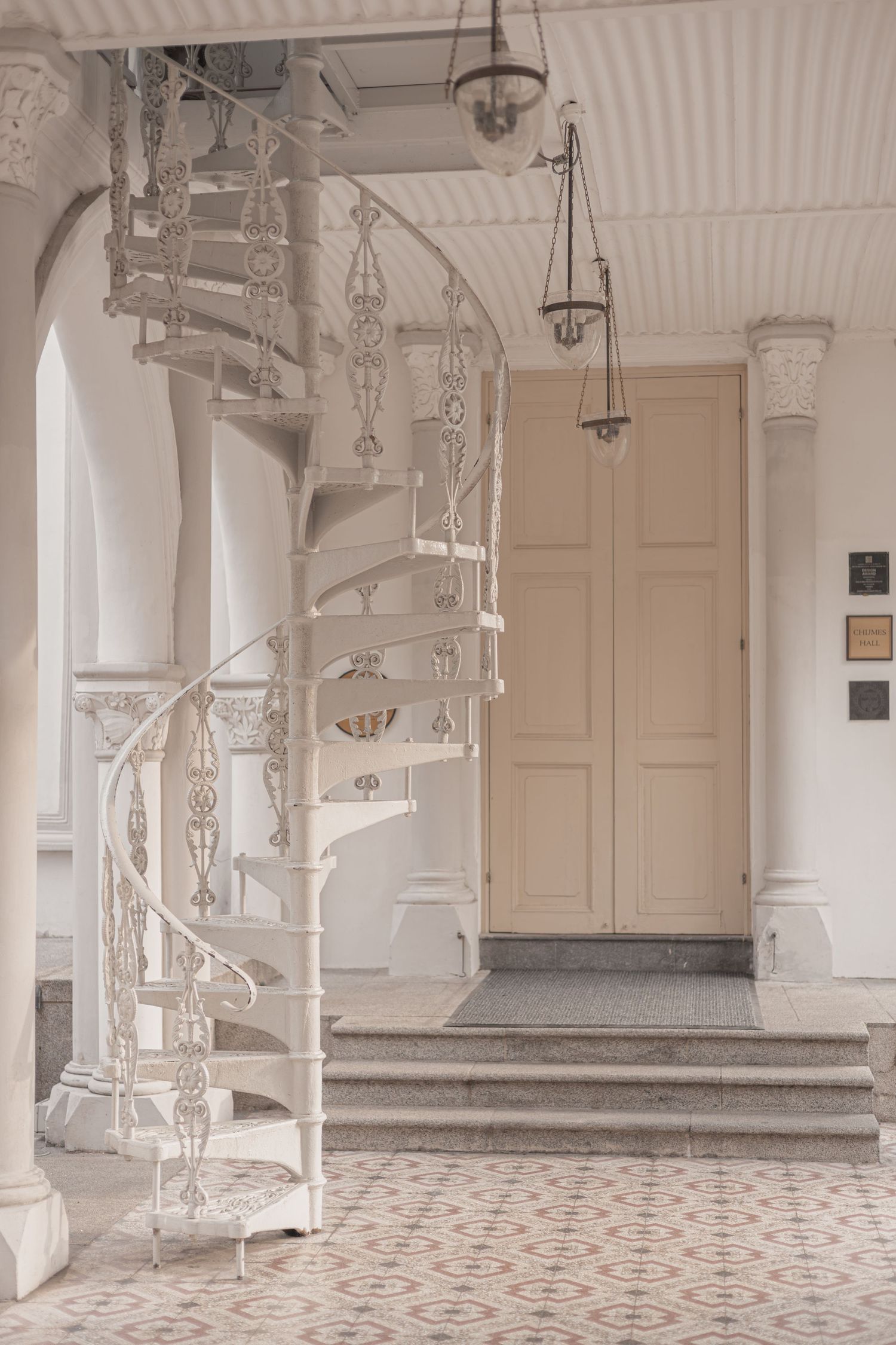 Elegant white spiral staircase with ornate iron railings in a classic interior with patterned tile floors and arched columns.