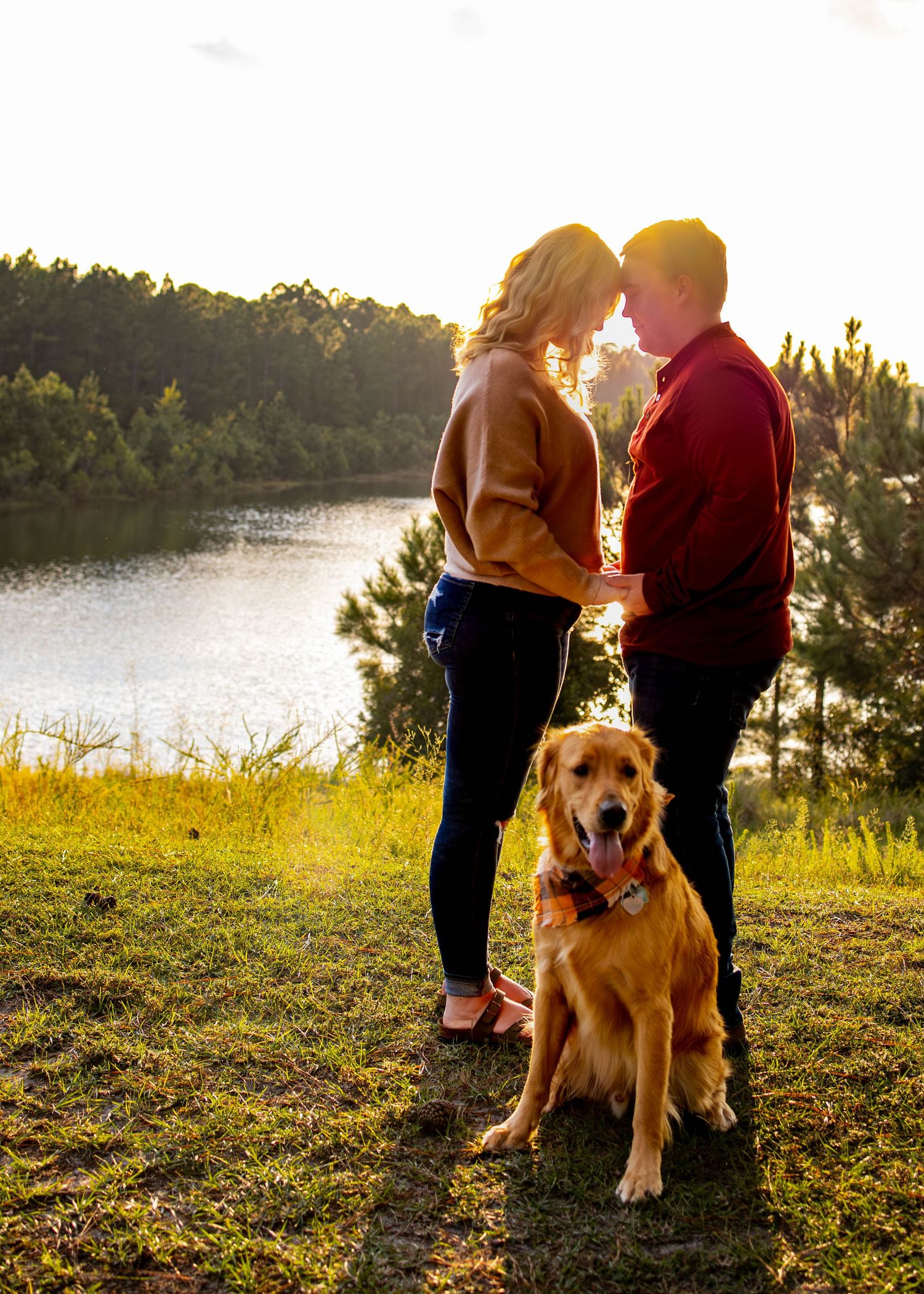 Golden retriever poses with couple during sunset photoshoot by a lake.