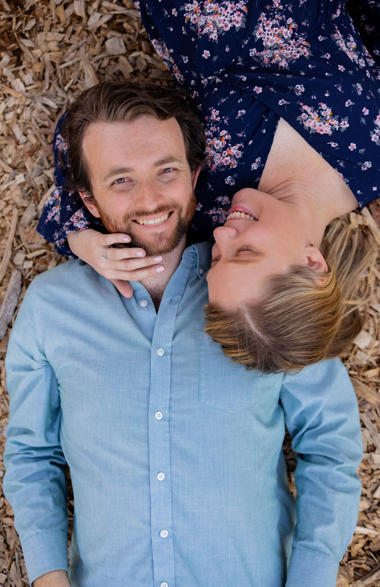 Playful couple lying on autumn leaves in casual blue and floral outfits.