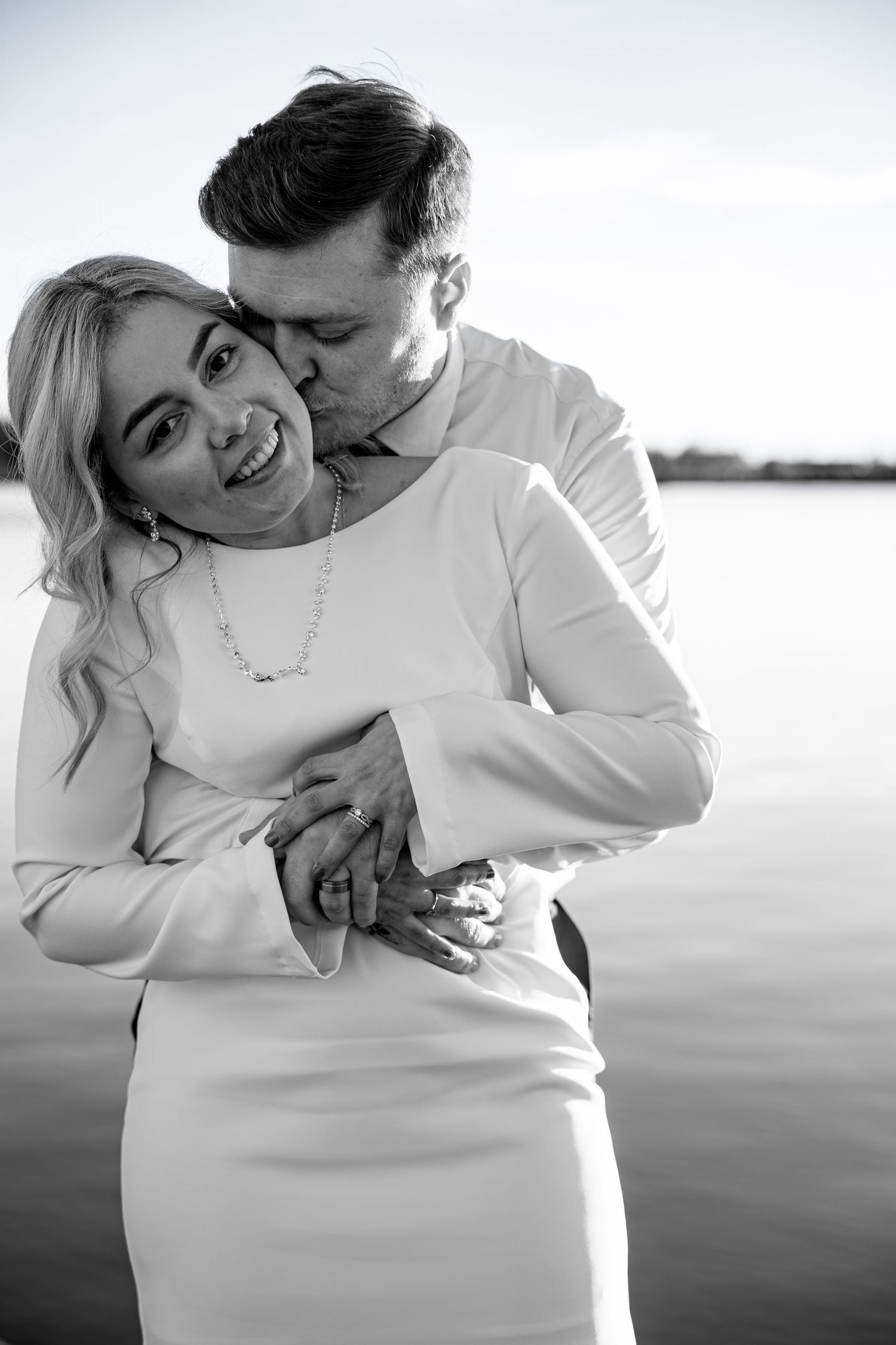 Intimate couple portrait session in white outfits against a serene waterfront backdrop.