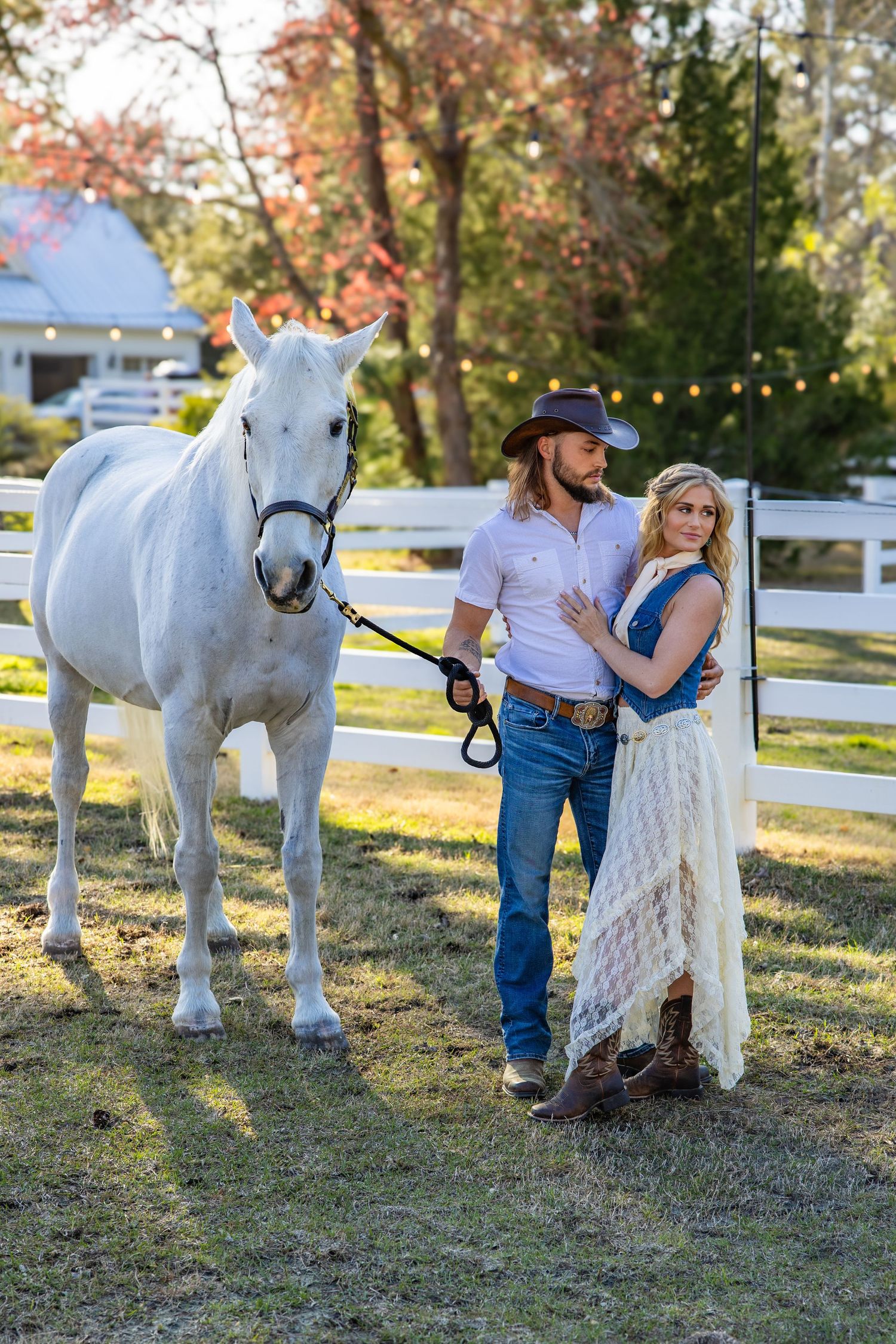 A couple poses with a beautiful white horse in a pastoral setting during a romantic autumn photoshoot.