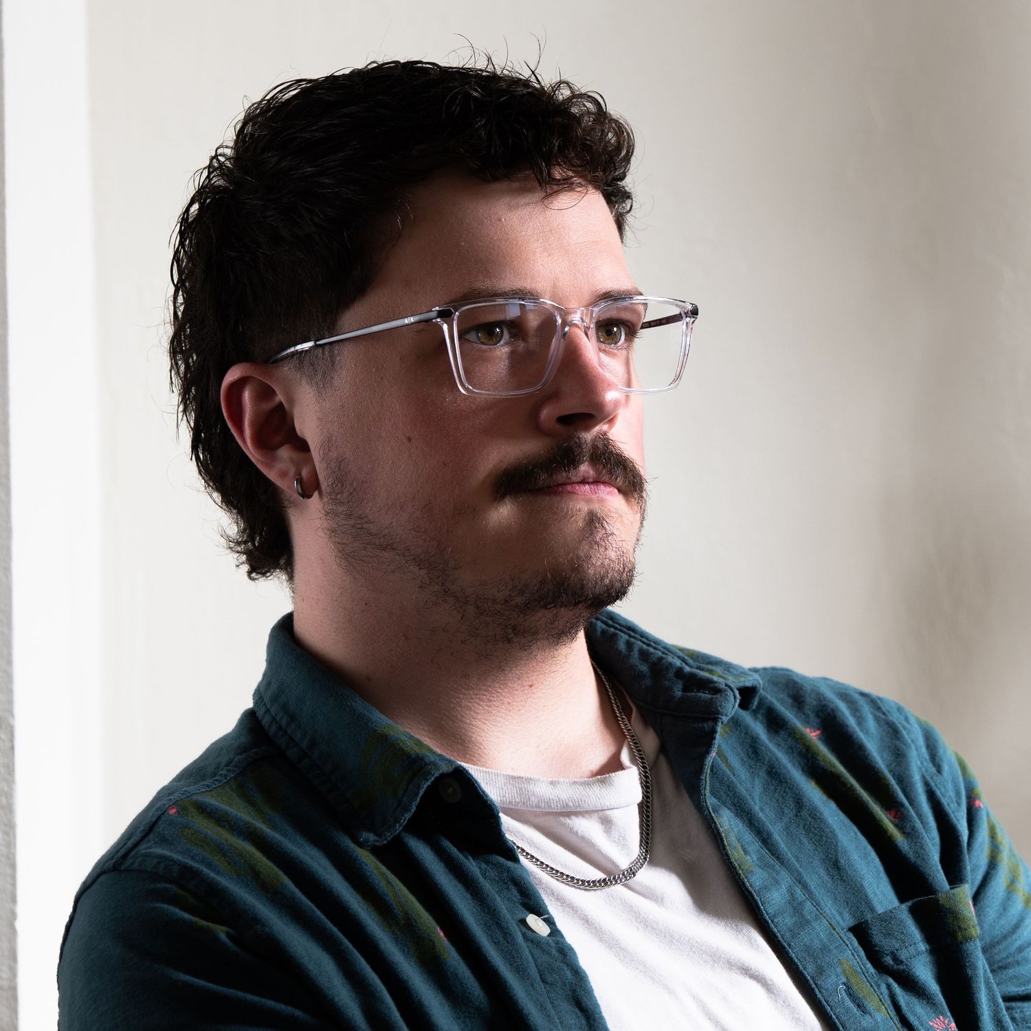 Portrait against white wall wearing teal jacket and glasses.